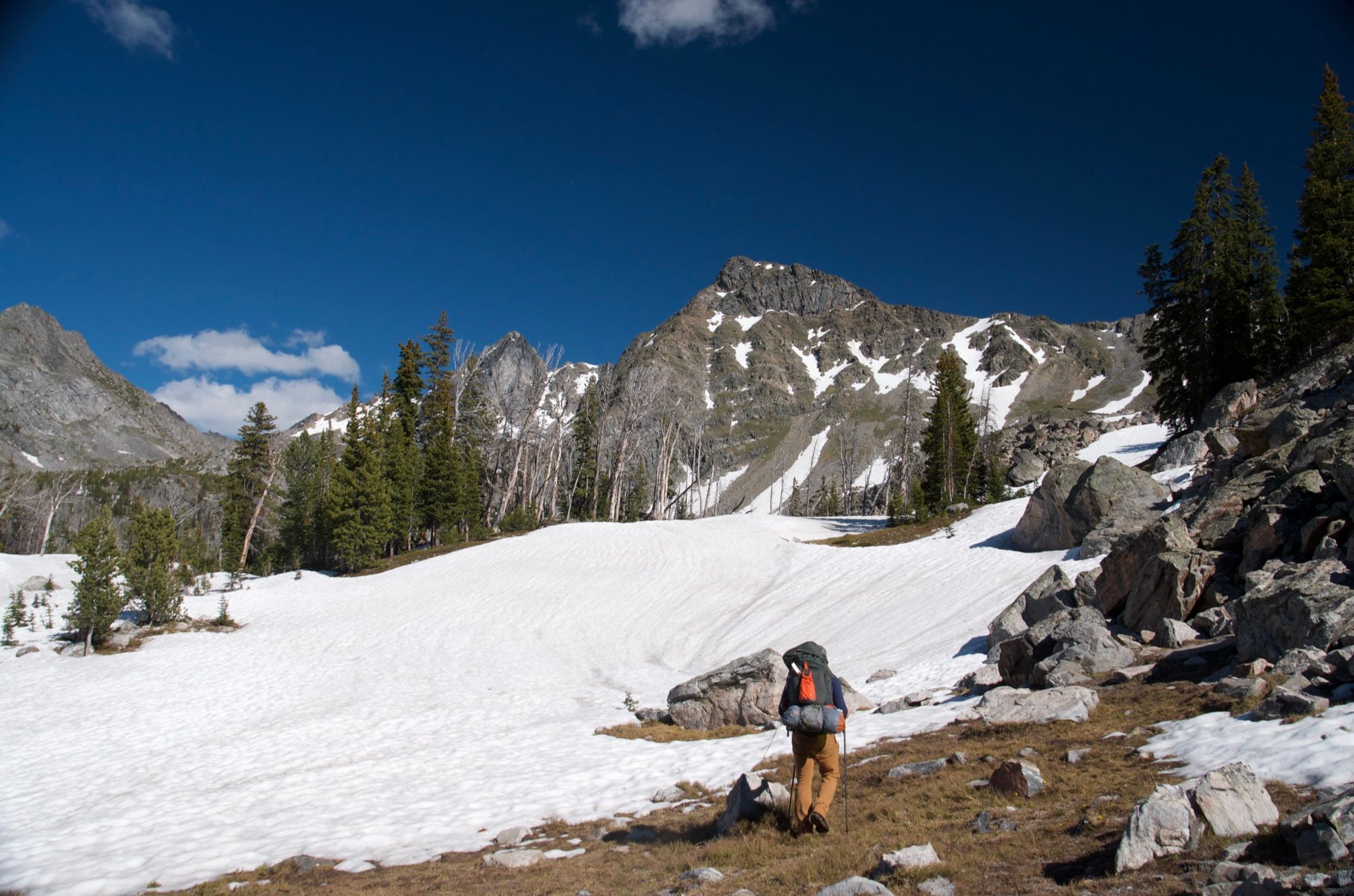 Backpacker traversing snowfield below dramatic Spanish Peaks