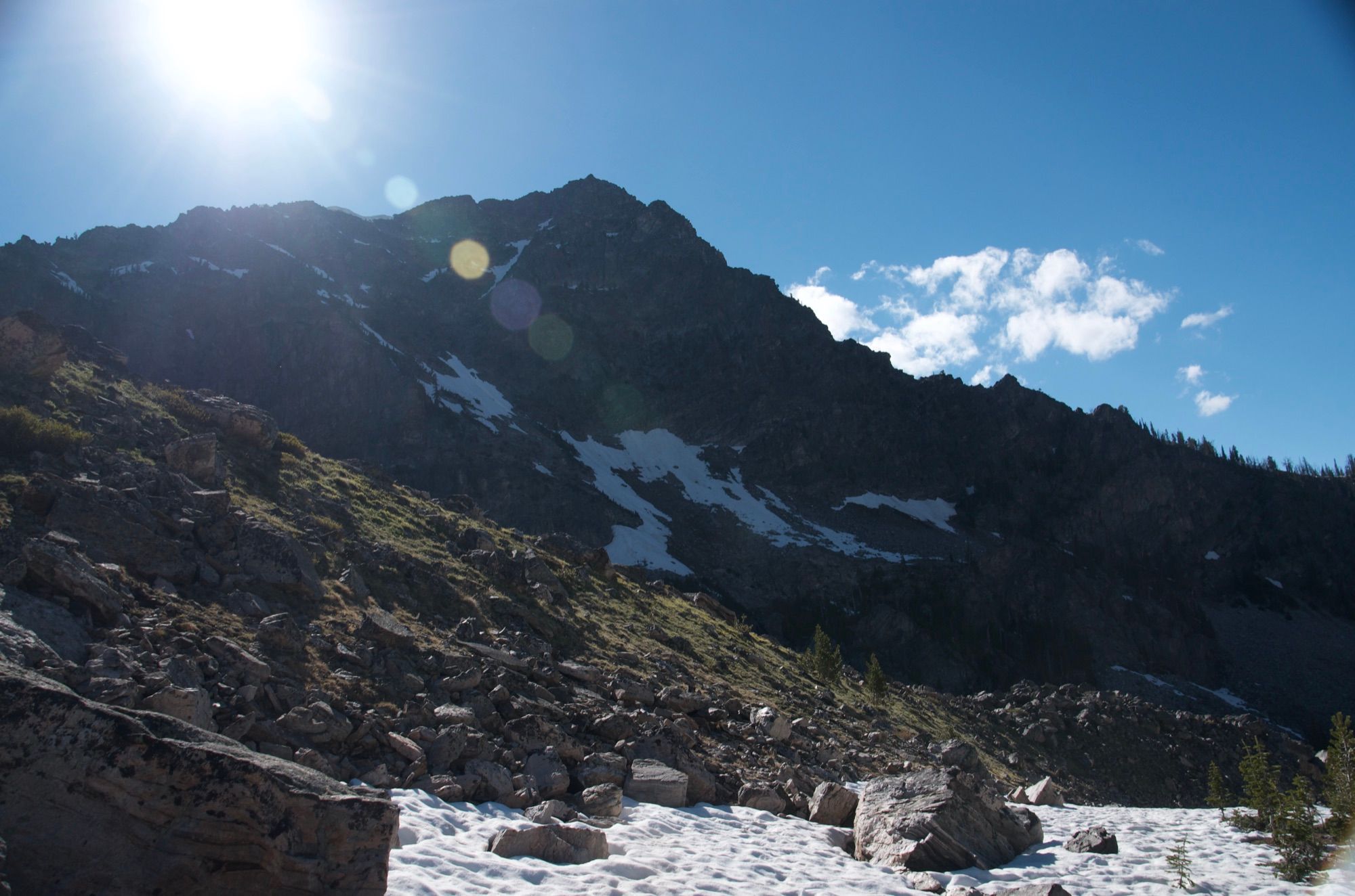 Rugged peak with snow patches and sun flare above rocky slope