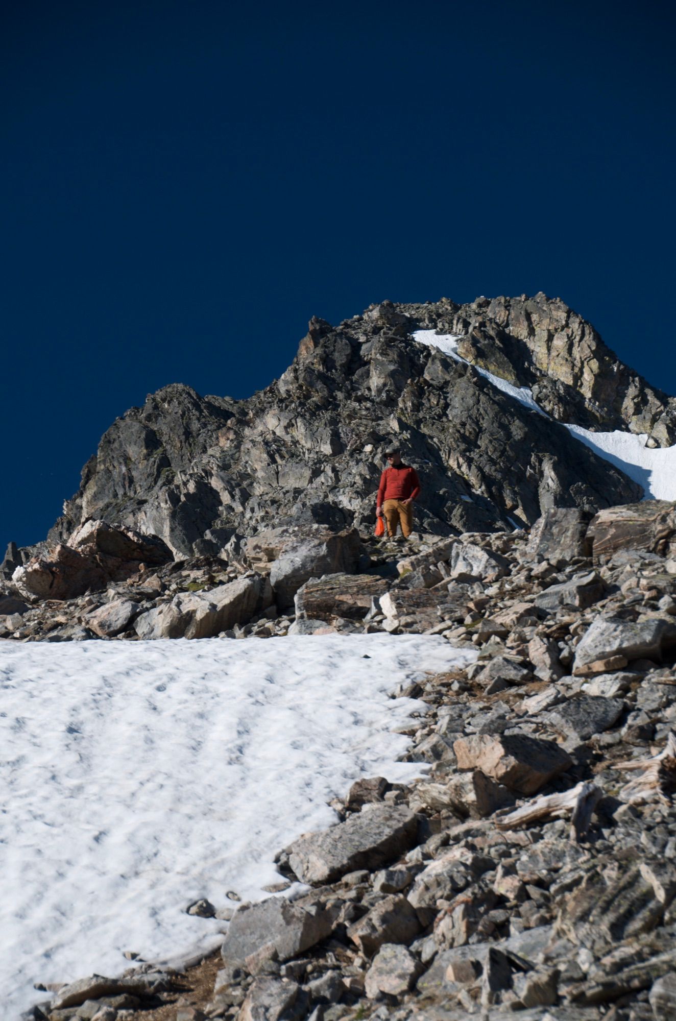 Hiker scrambling on rocky ridge above snowfield