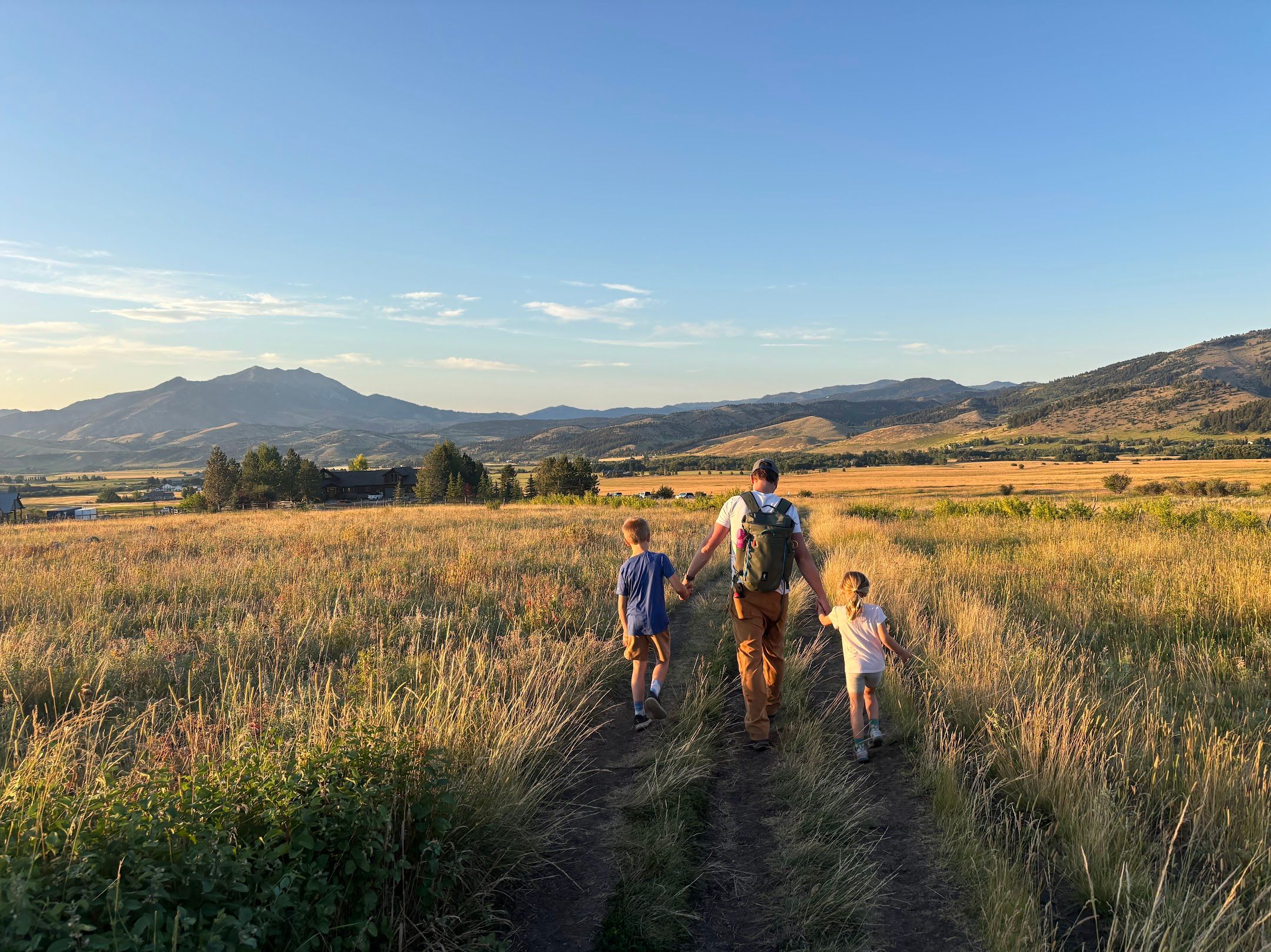 Family with two children hiking through a golden meadow at sunset near Bozeman with the Gallatin Range in the distance