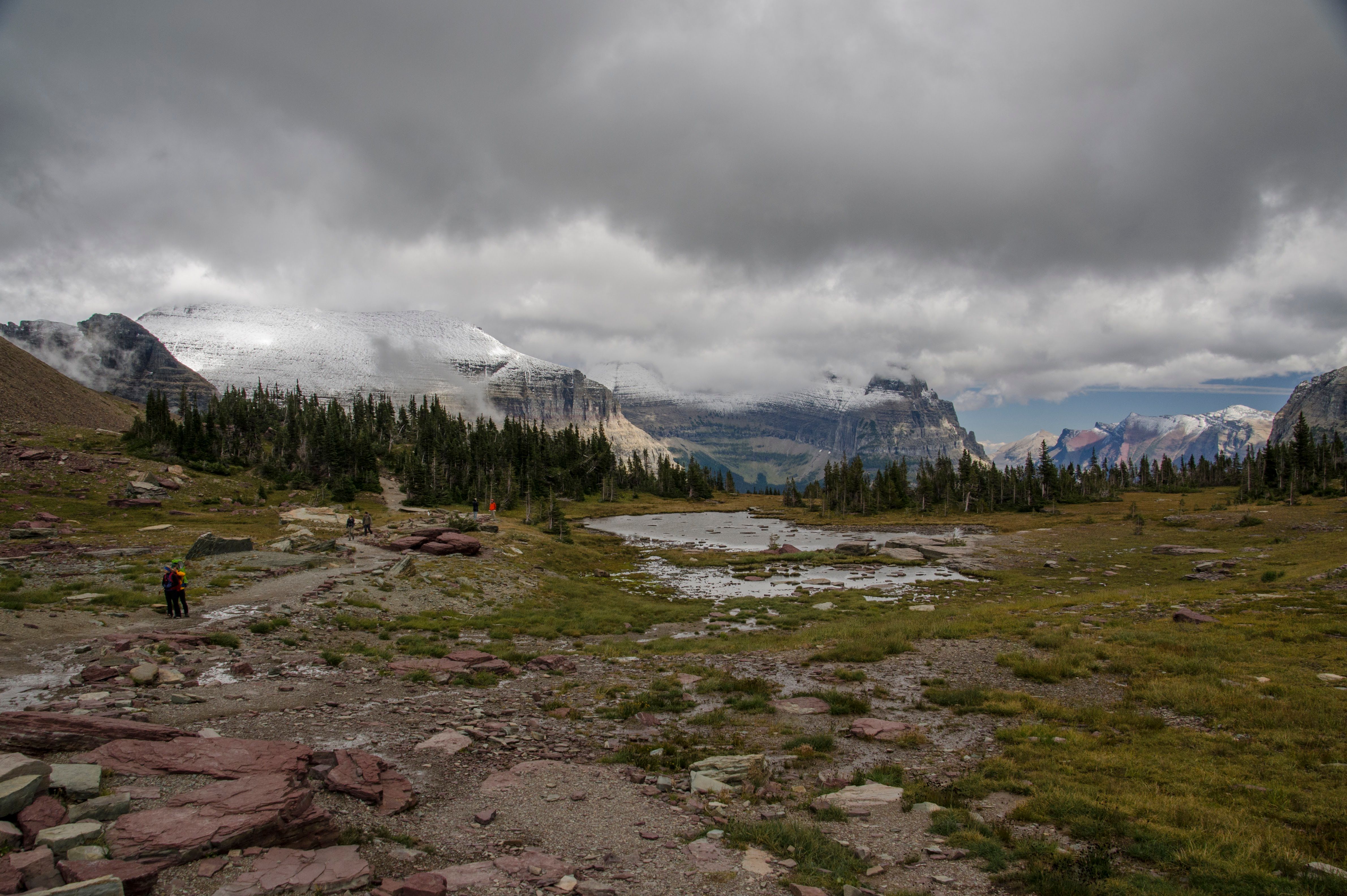 Wide alpine basin with small pond and hiker on rocky trail