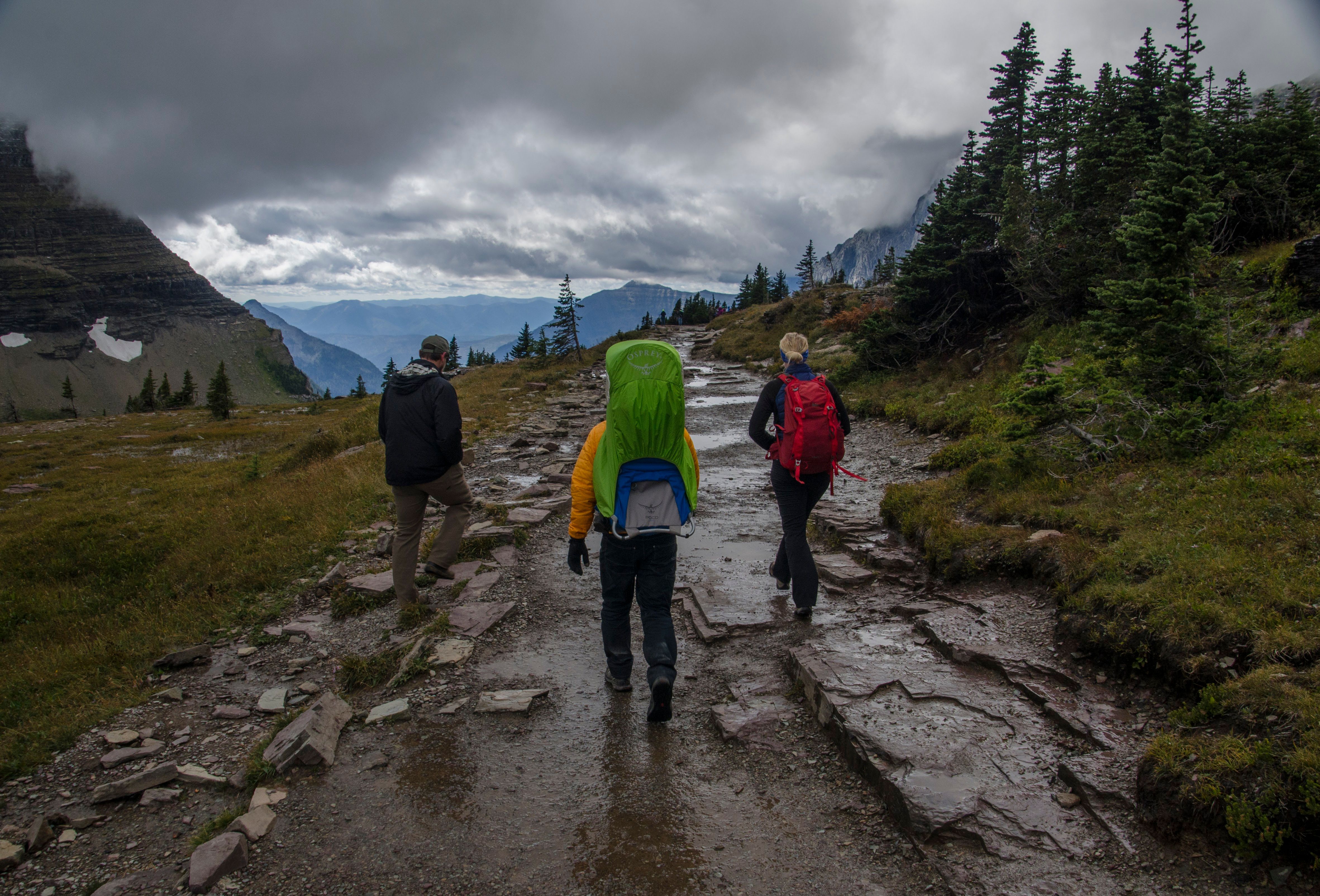 Three hikers in rain gear on wet rocky trail with mountains behind