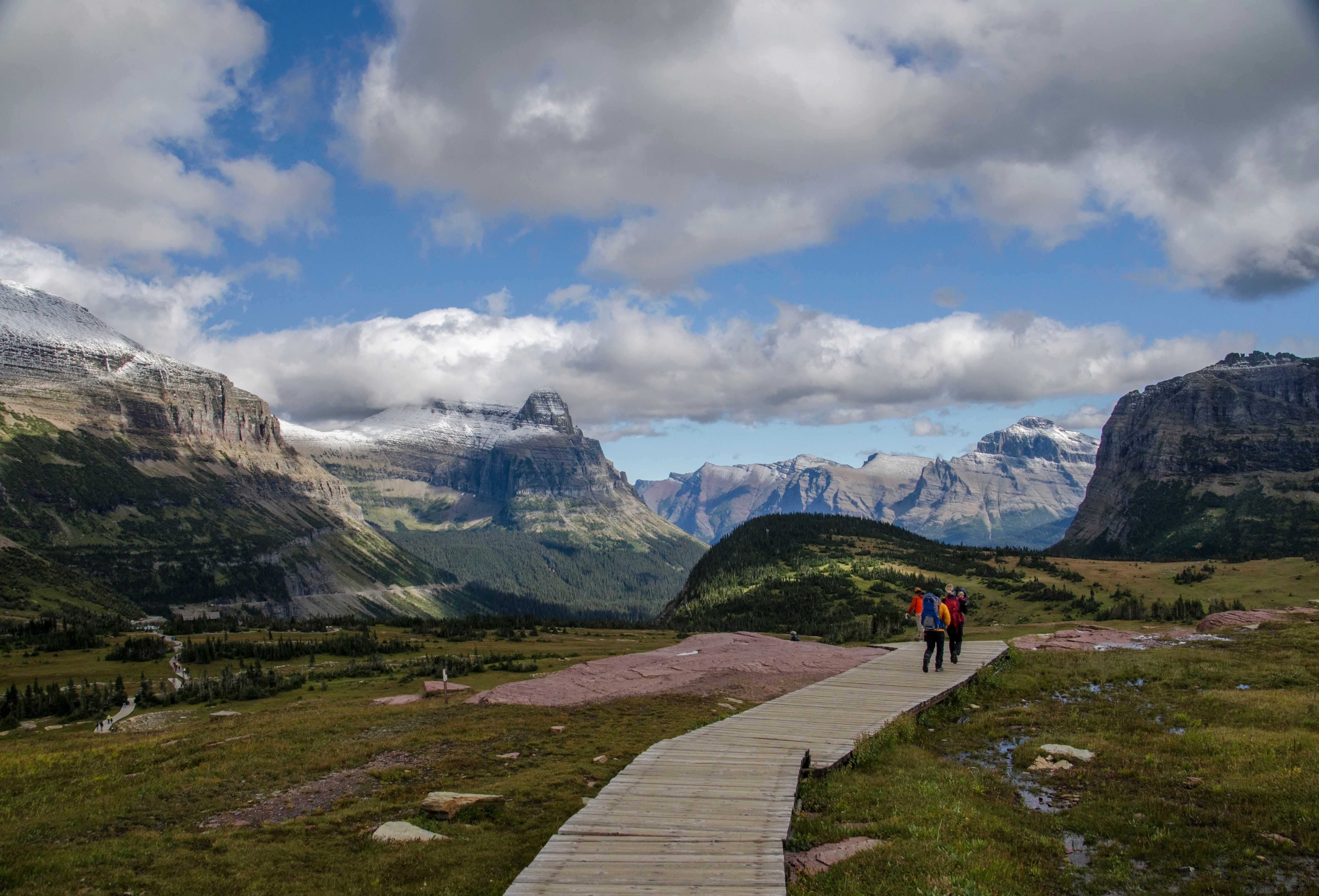 Two hikers on boardwalk trail with snow-capped peaks framing the valley ahead