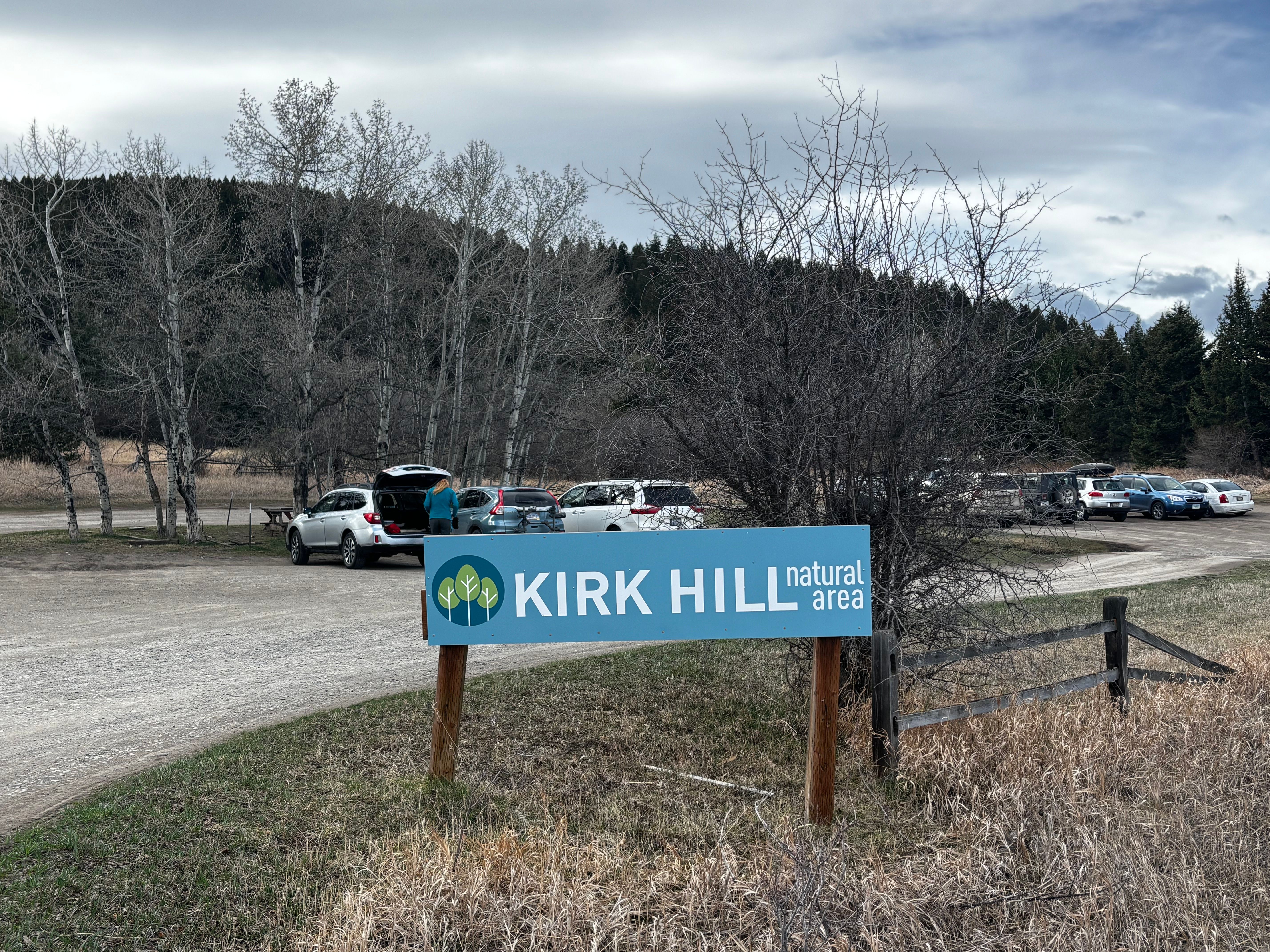 Kirk Hill Natural Area sign at the entrance to the gravel trailhead parking lot with forested hillside beyond