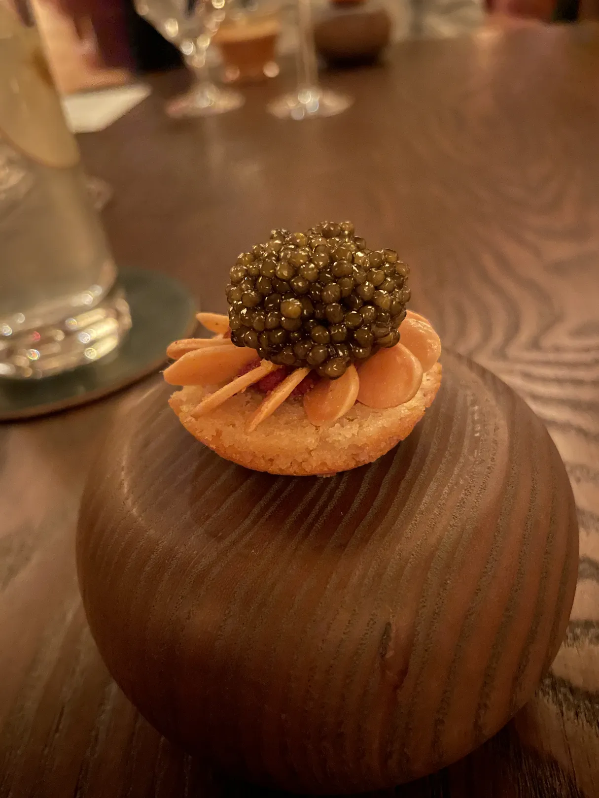 Elegant caviar dish with delicate petals on a wooden presentation stand at M by The Alinea Group