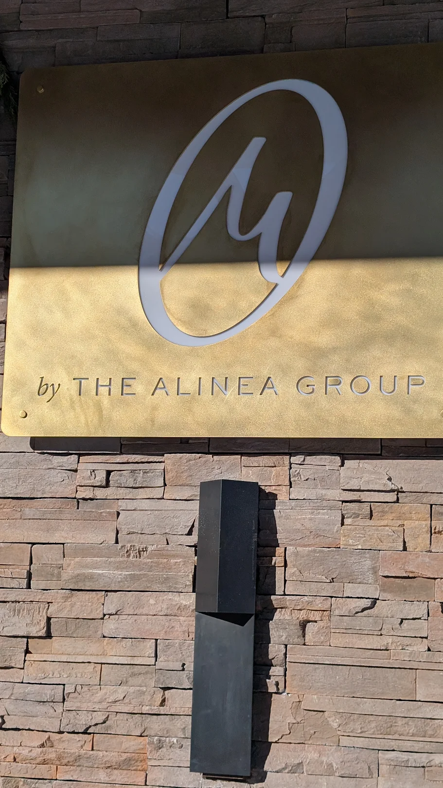 M by The Alinea Group gold sign on stone wall at Big Sky Resort