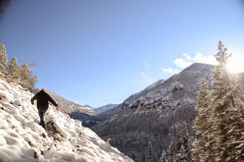 Hiker climbing snowy slope with Hyalite Canyon mountain views