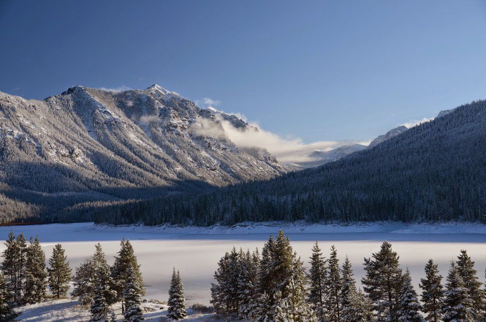 Frozen Hyalite Reservoir with dramatic mountain backdrop and low clouds