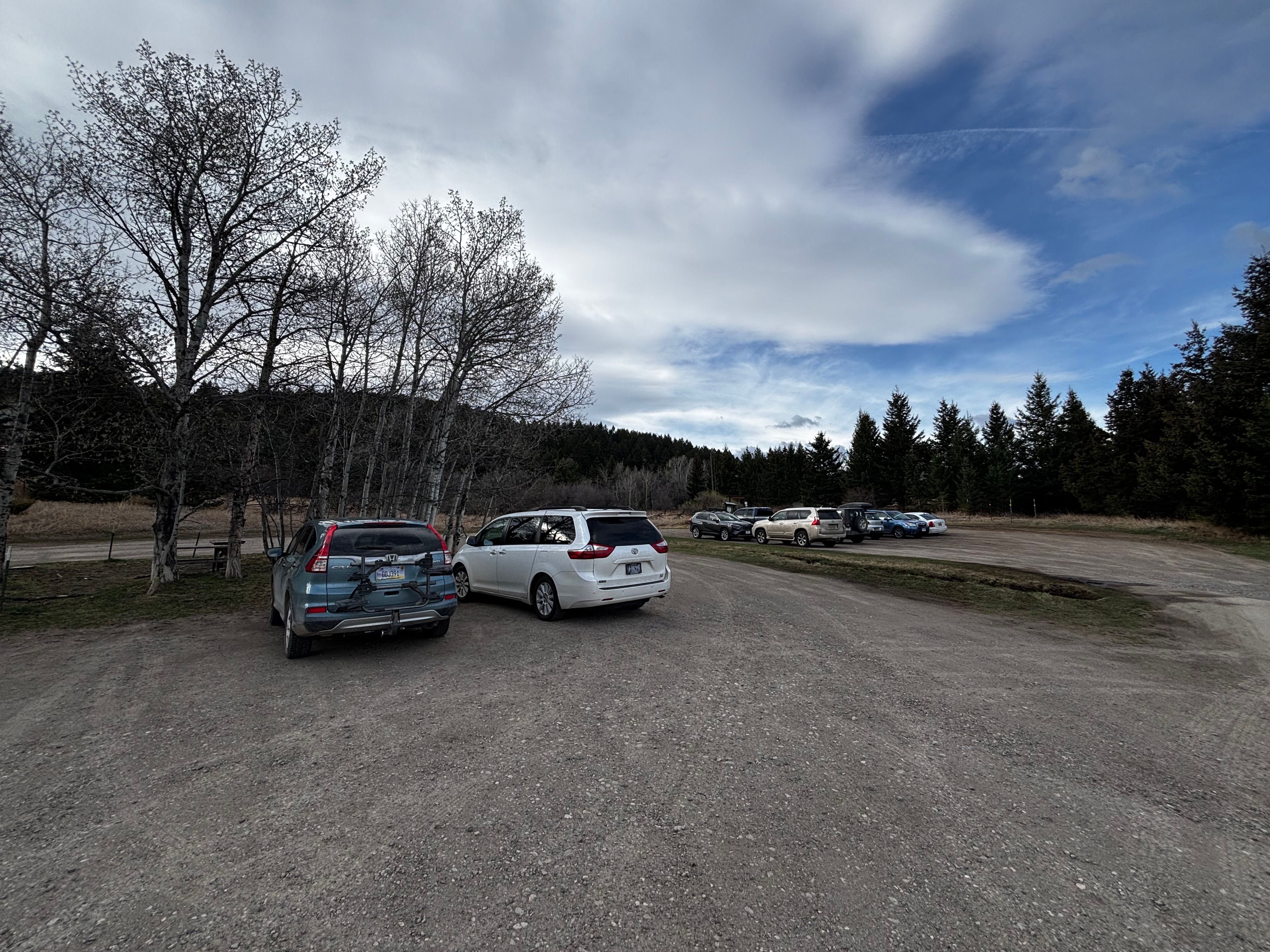 Large gravel parking lot at Kirk Hill Natural Area with aspen trees and forested hillside in the background