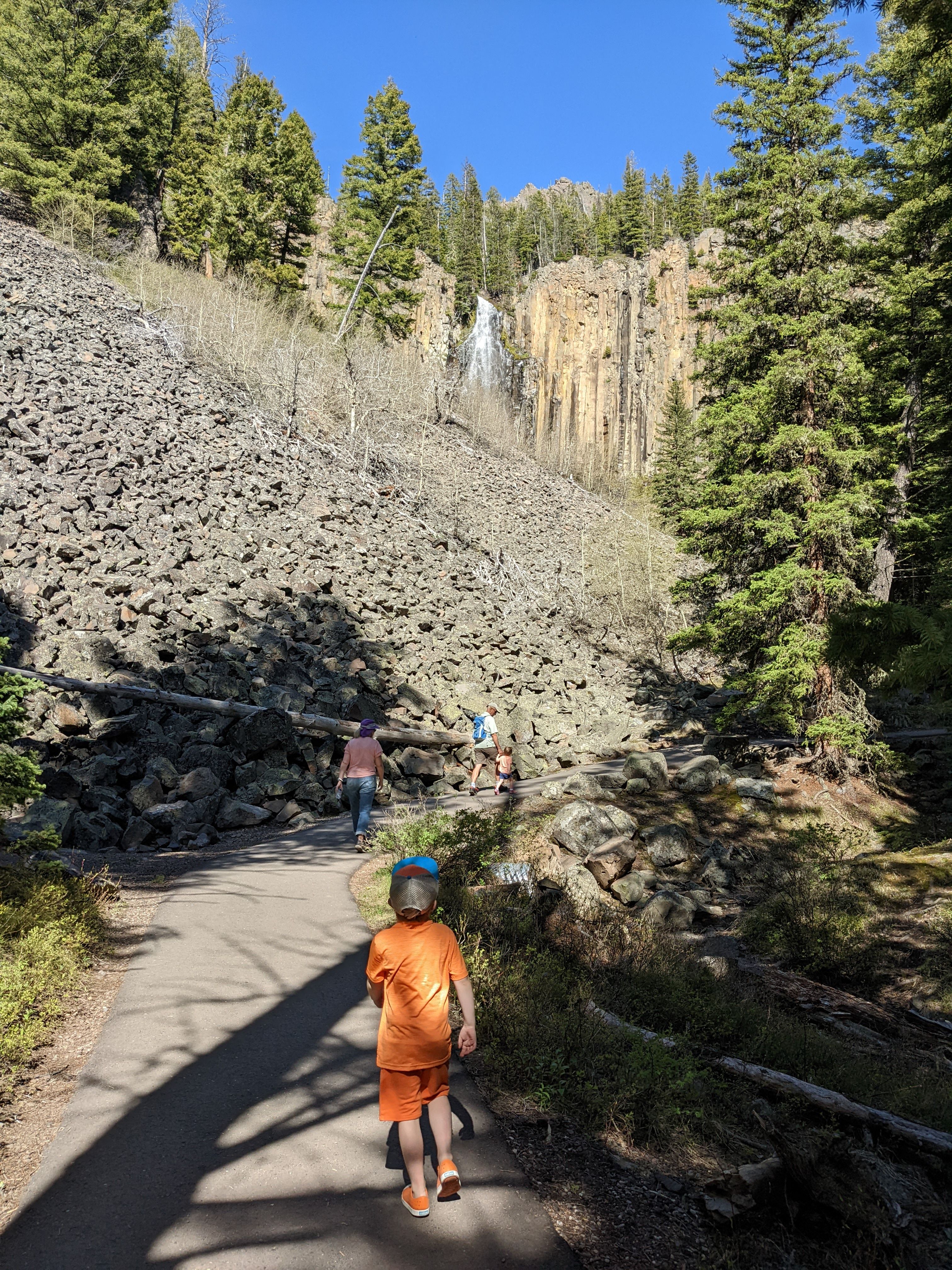 Child walking on the paved Palisade Falls trail approaching the columnar basalt cliffs and waterfall