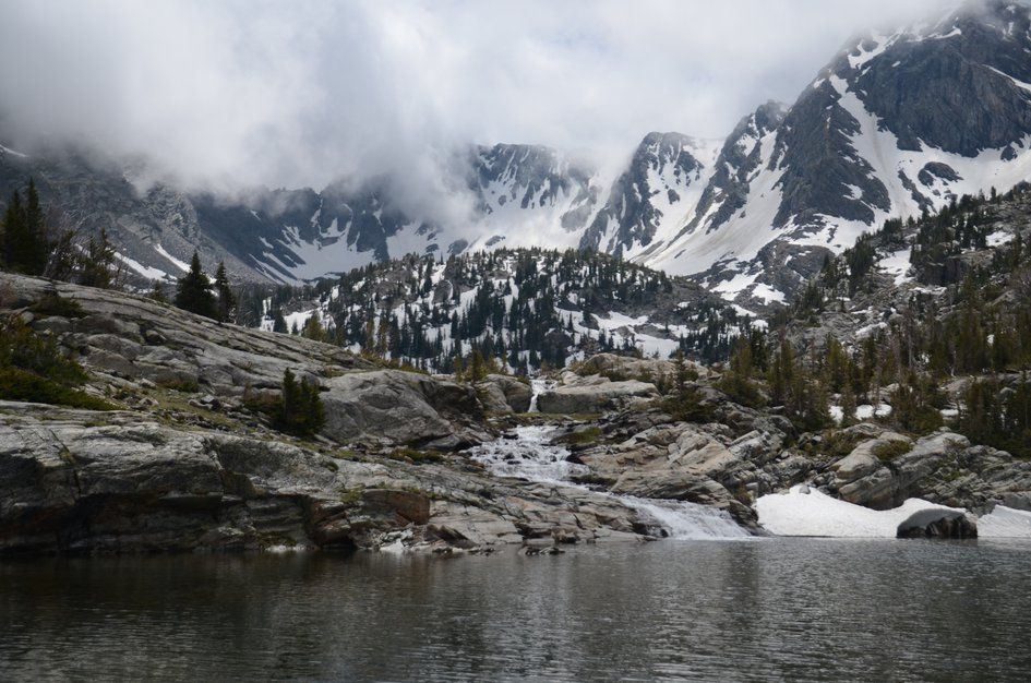 Pine Creek Lake with waterfall inlet and snow-capped Absaroka peaks in clouds