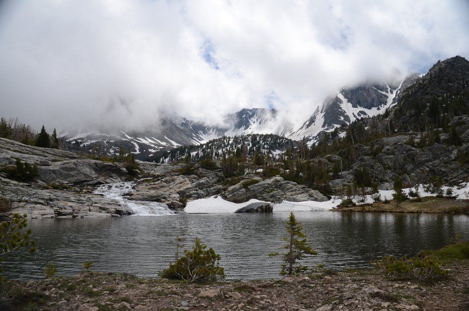 Pine Creek Lake with waterfall, snow cornice, and jagged peaks in swirling clouds