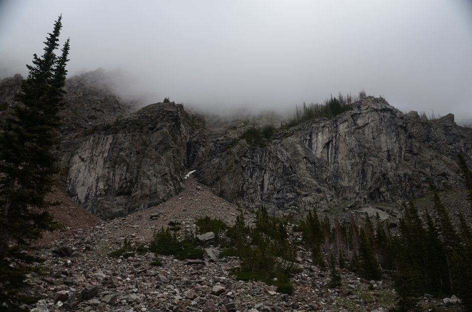 Massive granite headwall with talus slope disappearing into low clouds