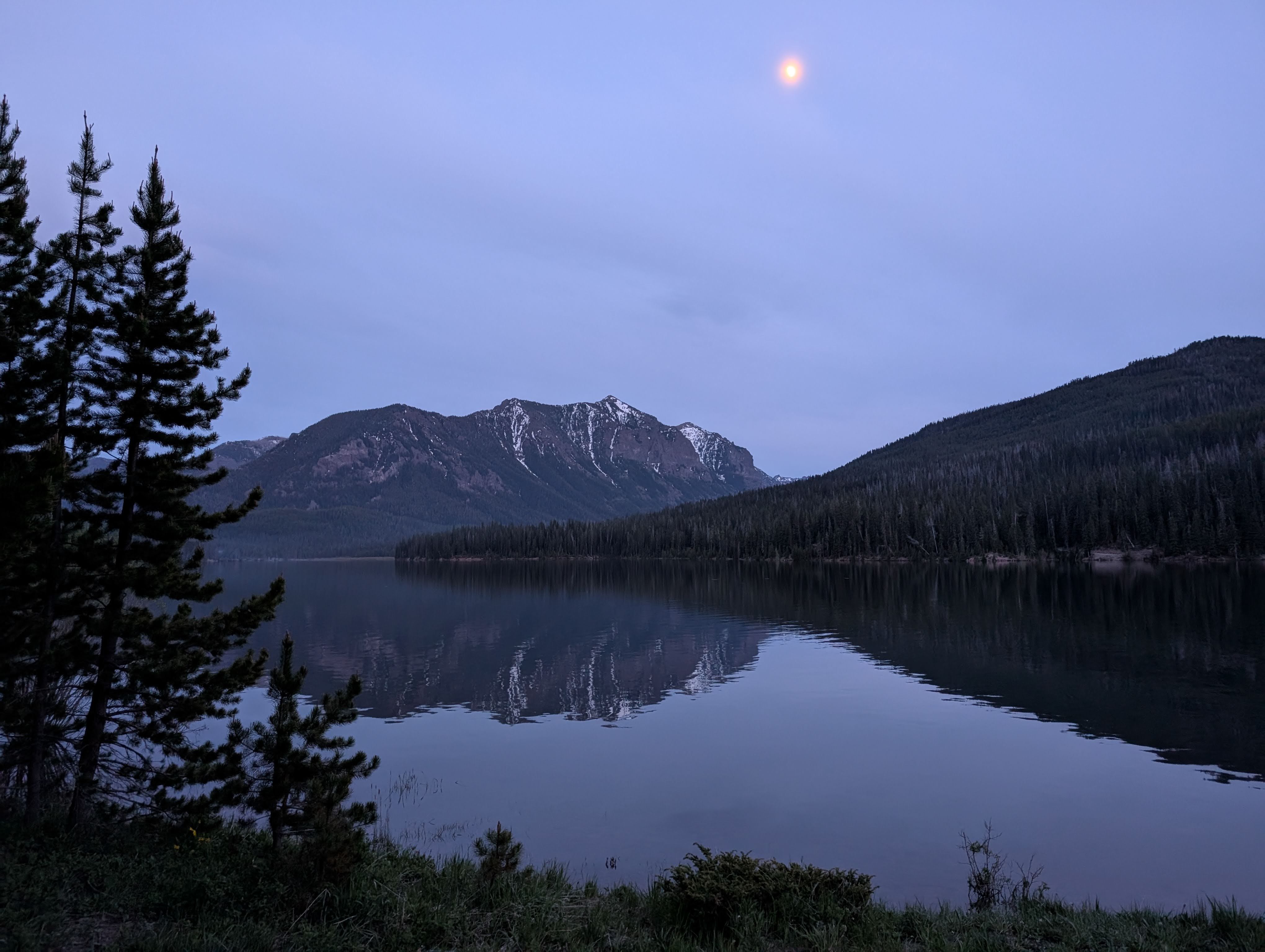 Hyalite Reservoir at dusk with crescent moon rising over silhouetted mountains