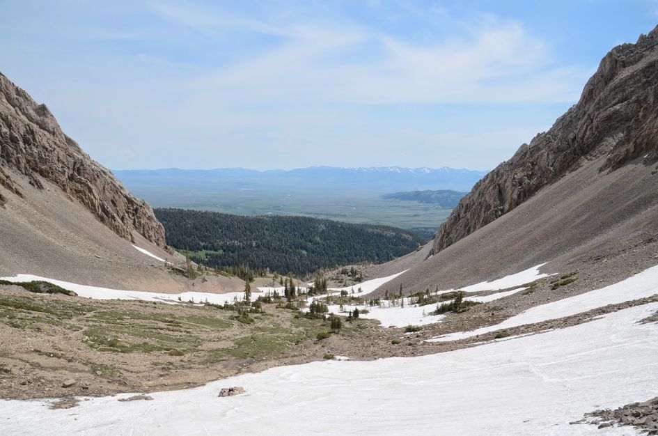 Snow-filled alpine basin between steep limestone walls with Gallatin Valley beyond
