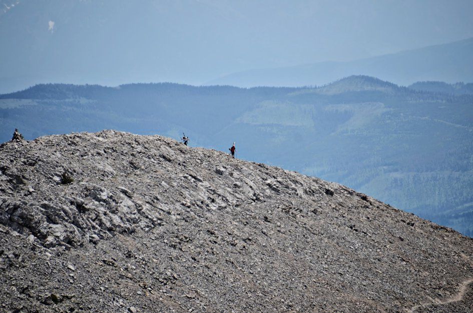 Tiny hikers on distant rocky ridge with hazy mountain ranges beyond