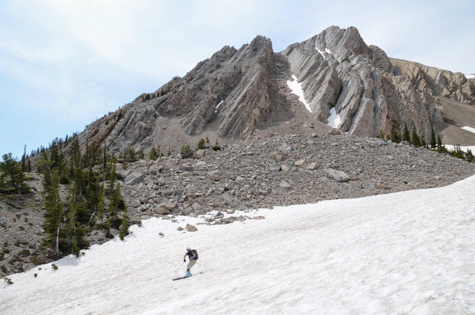 Skier carving turns below massive limestone cliffs and talus slope