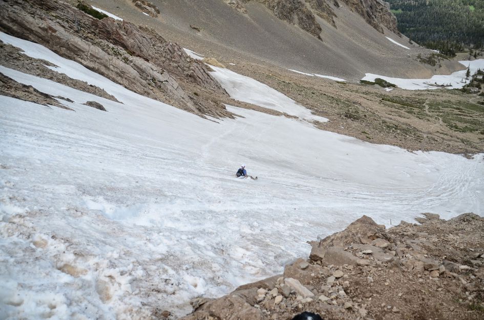 Person glissading down steep snow slope in alpine basin