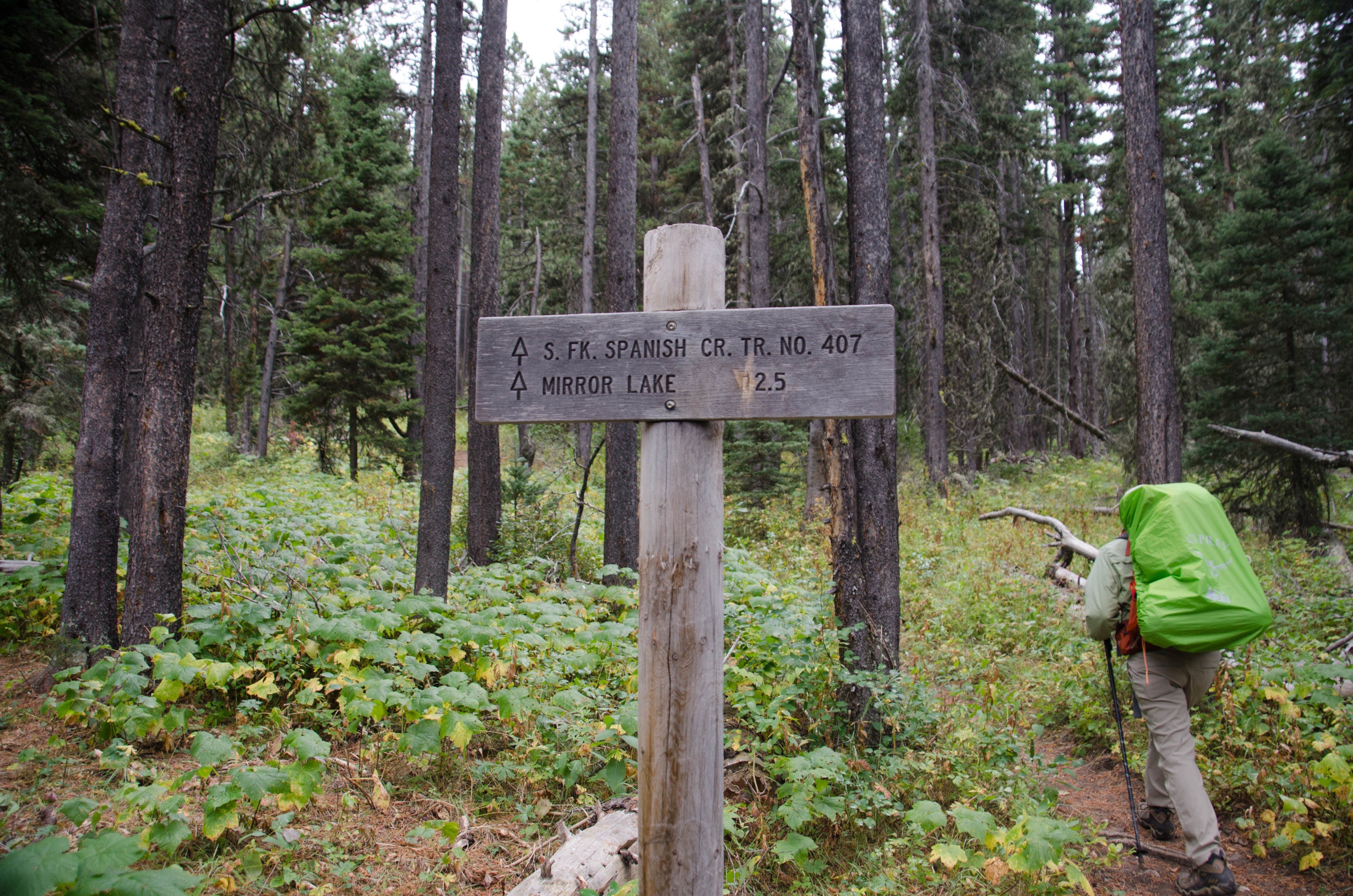 Trail sign showing Mirror Lake 2.5 miles with backpacker in dense forest
