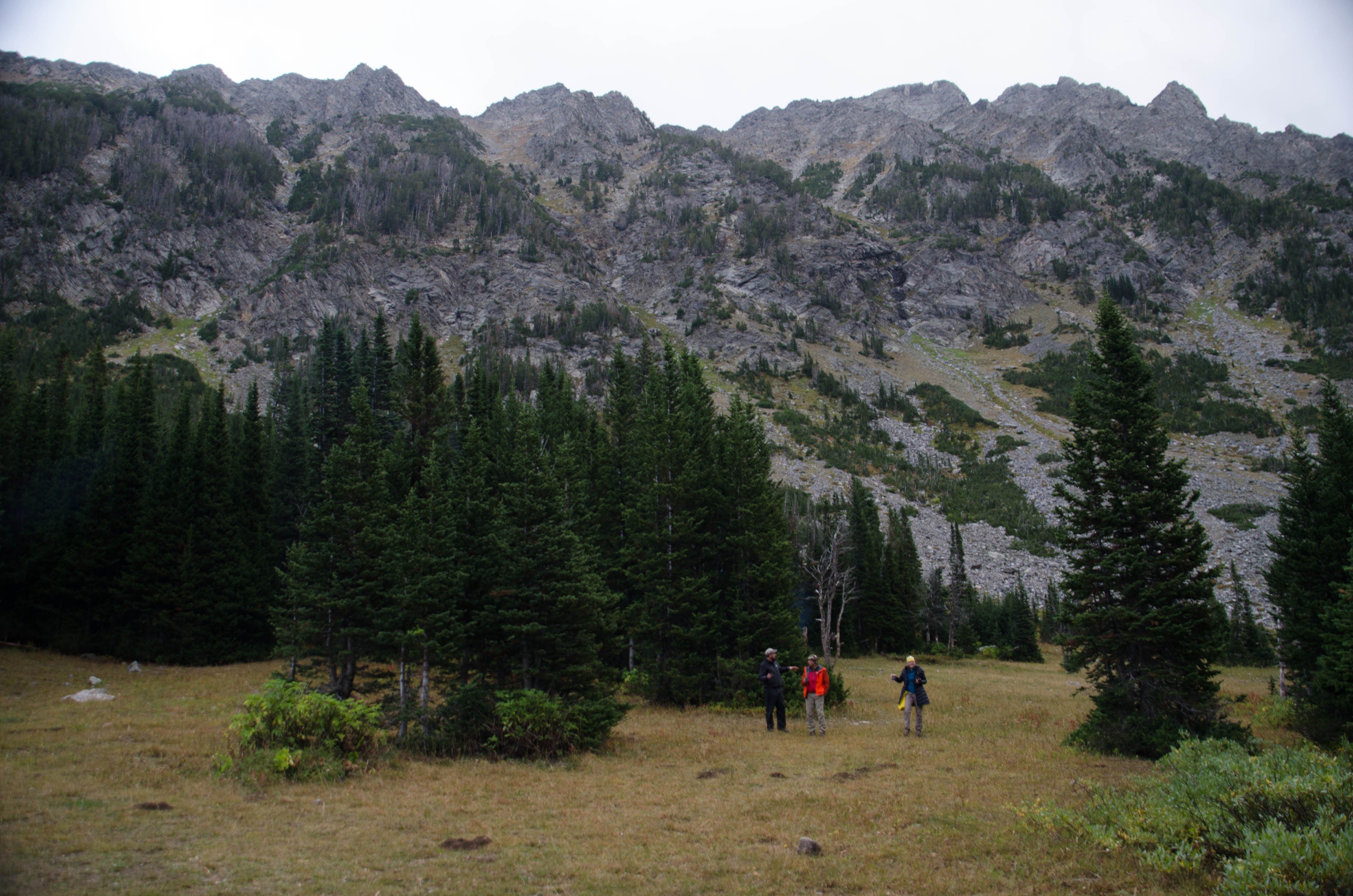 Three hikers crossing open meadow below jagged Spanish Peaks ridgeline