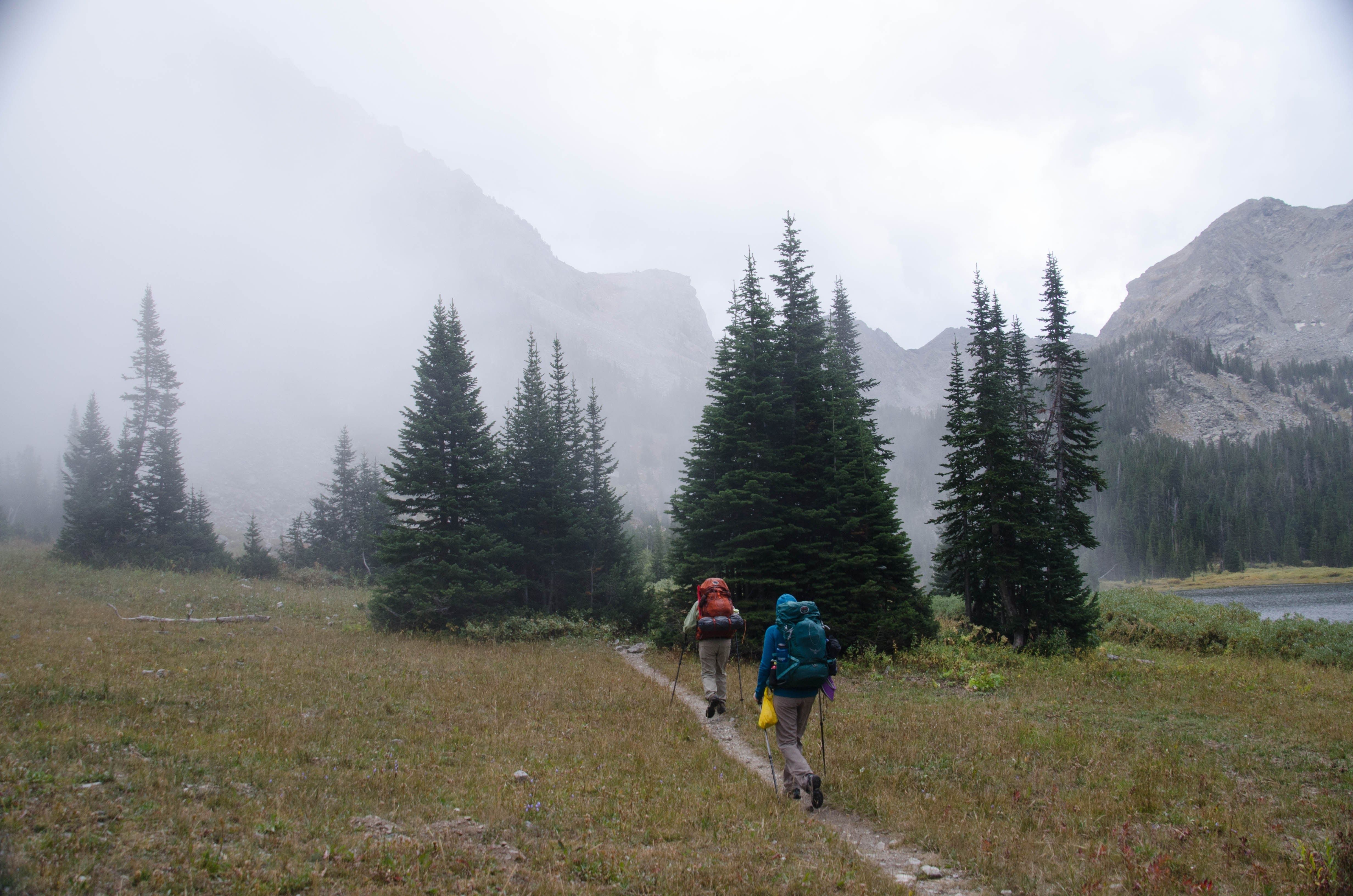 Two backpackers hiking through meadow toward Mirror Lake in fog