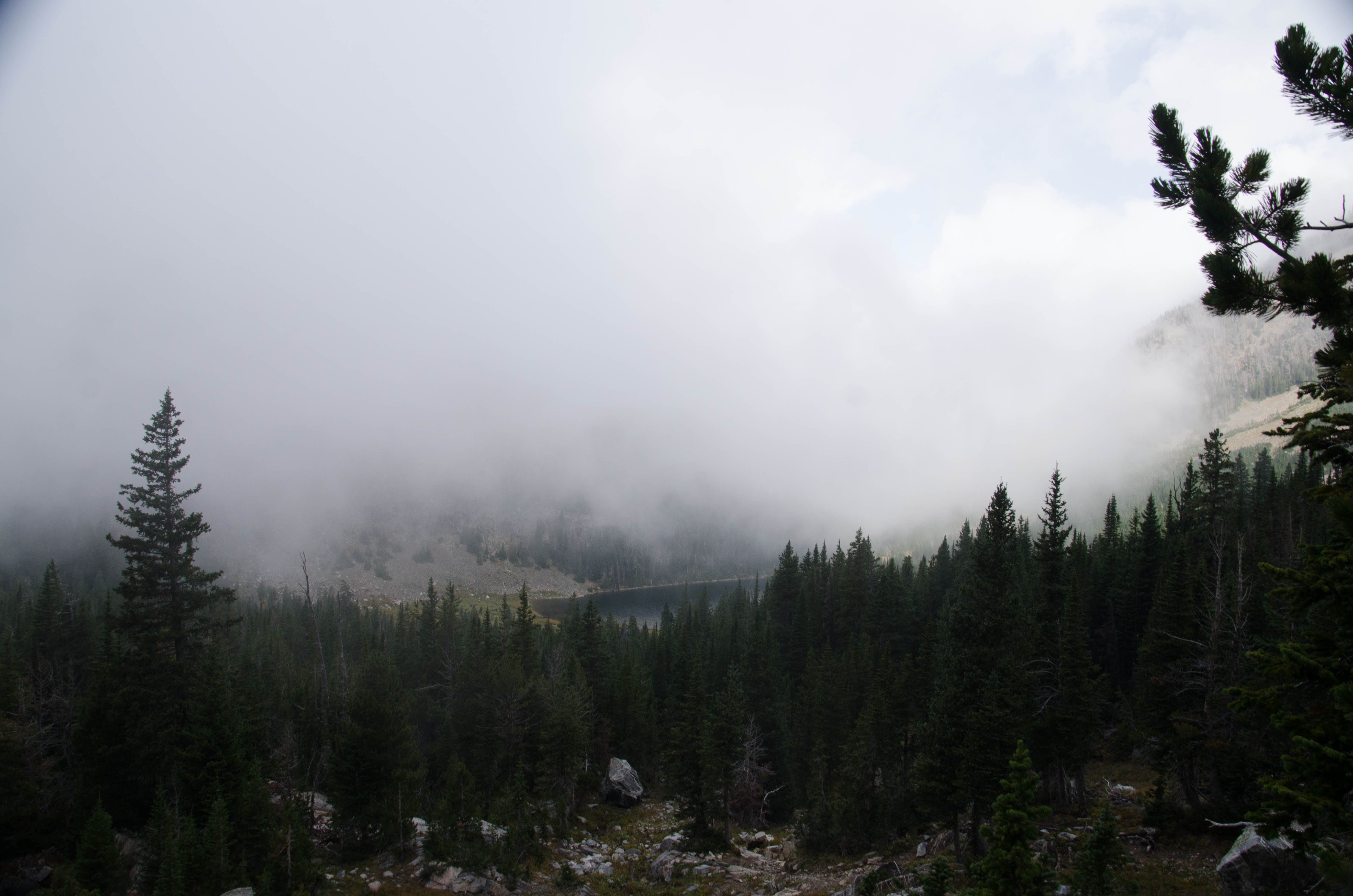Mirror Lake from elevated viewpoint with fog lifting over evergreen forest and rocky slopes