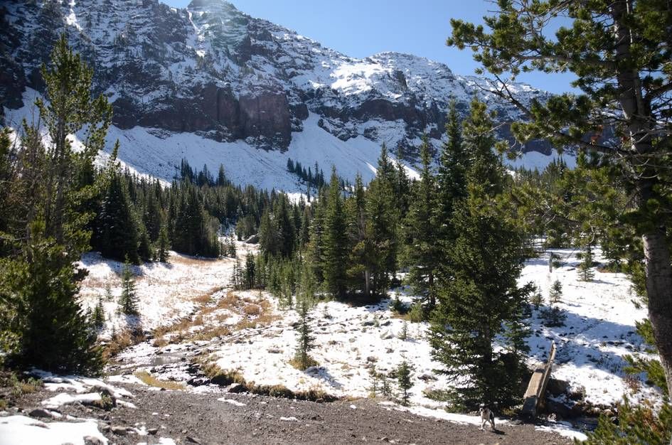 Snow-dusted alpine basin with creek crossing and jagged mountain peaks