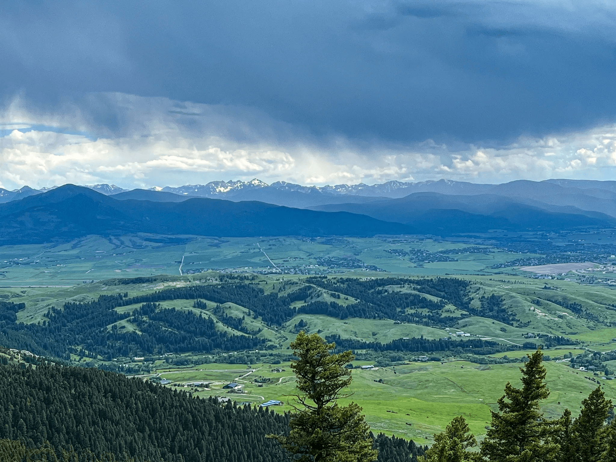 Wide Gallatin Valley view from Sypes Canyon with green foothills, distant mountains, and storm clouds