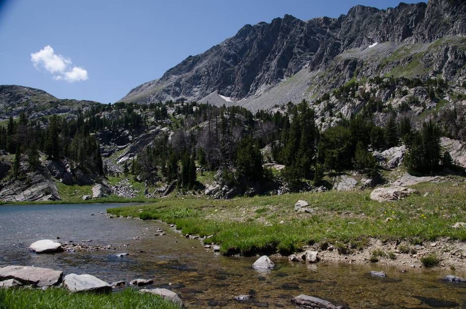 Clear alpine lake with grassy shoreline and steep cirque walls behind