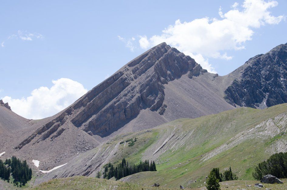 Tilted sedimentary rock layers forming dramatic pyramid peak above talus