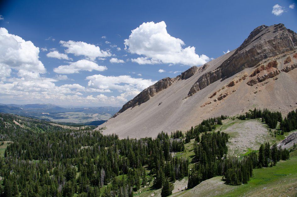 Massive talus slope and rocky peak above forested valley with distant views