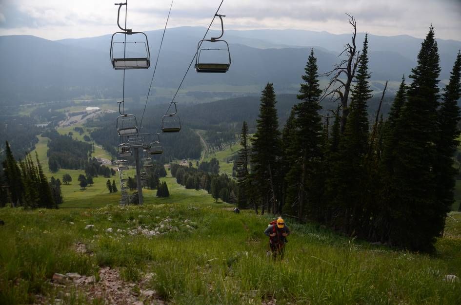 Hiker ascending grassy ski slope with chairlift and valley views behind