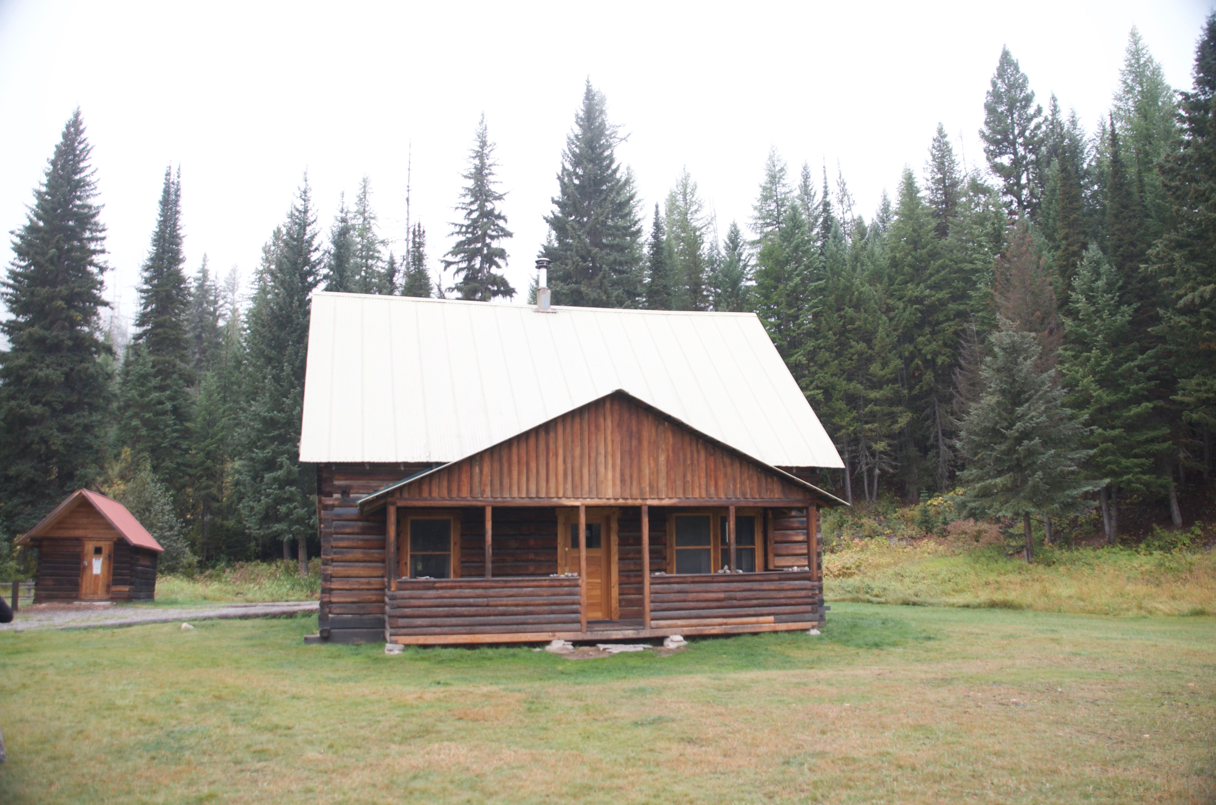 Wurtz Cabin front view showing the full exterior with pine trees and the small outbuilding to the left