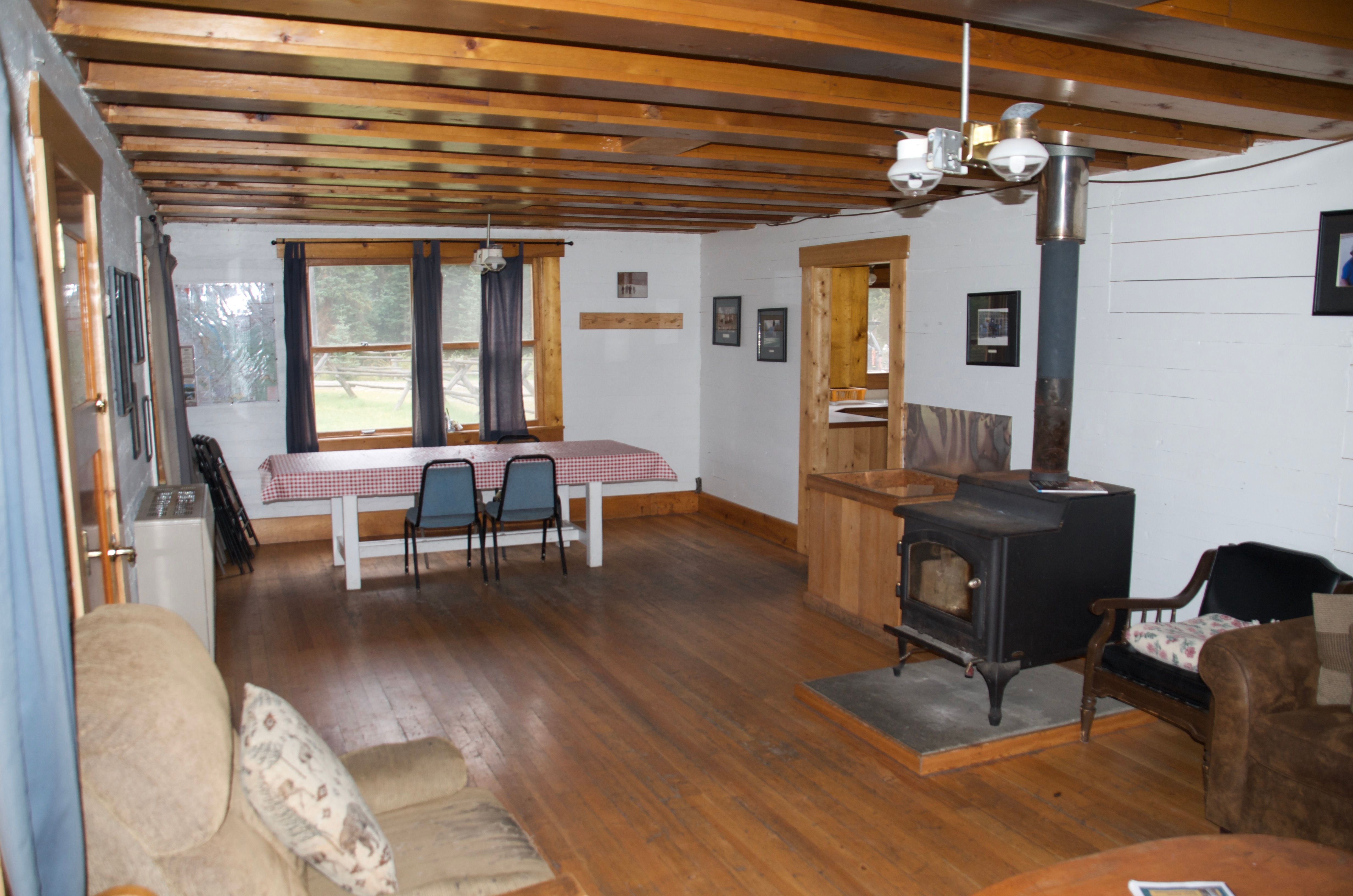 Wurtz Cabin living room from the other end, showing the dining area, wood stove, and exposed beam ceiling