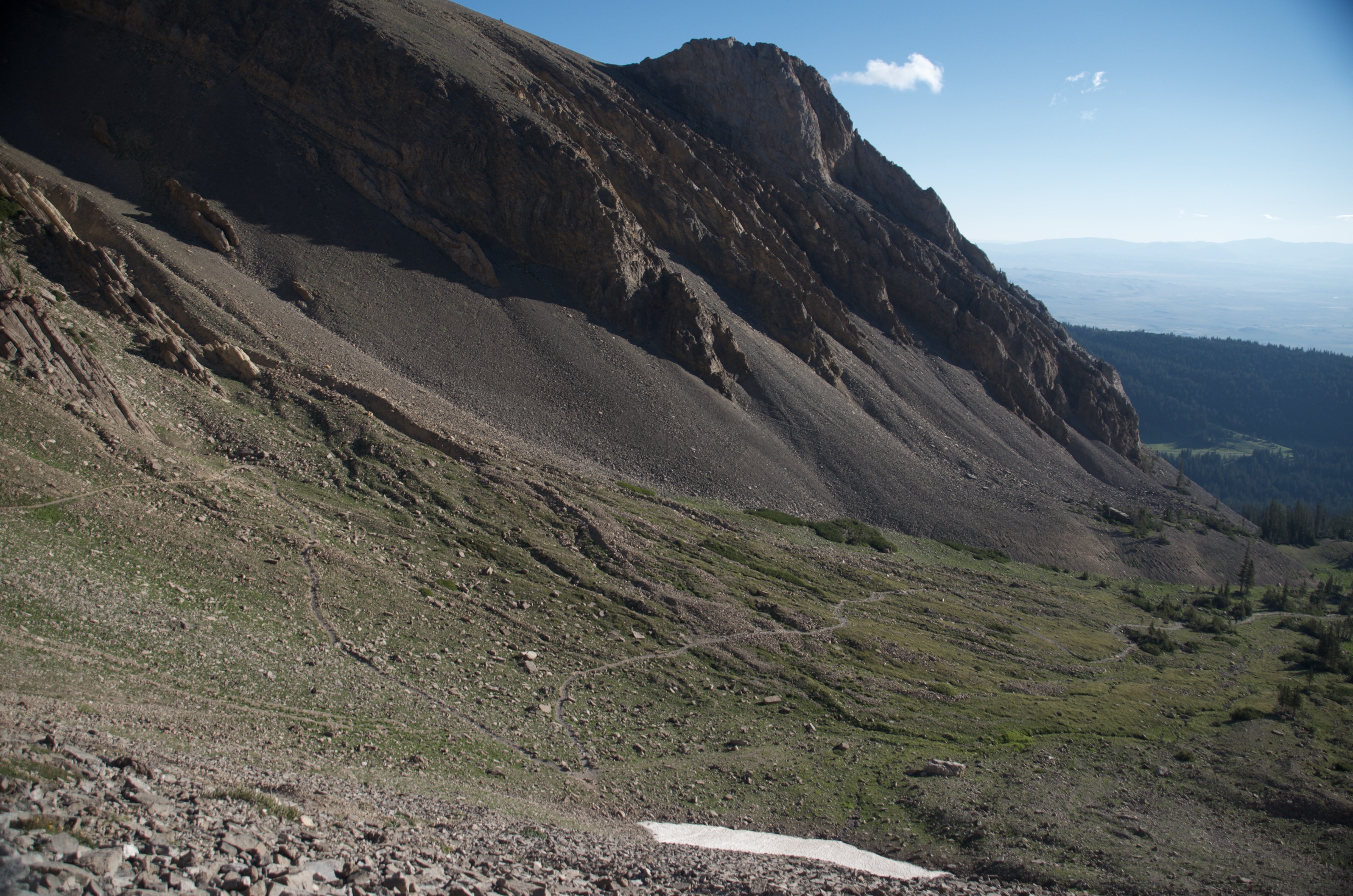 Steep talus traverse below a massive cliff face on the Bridger Ridge with the valley visible through the open terrain