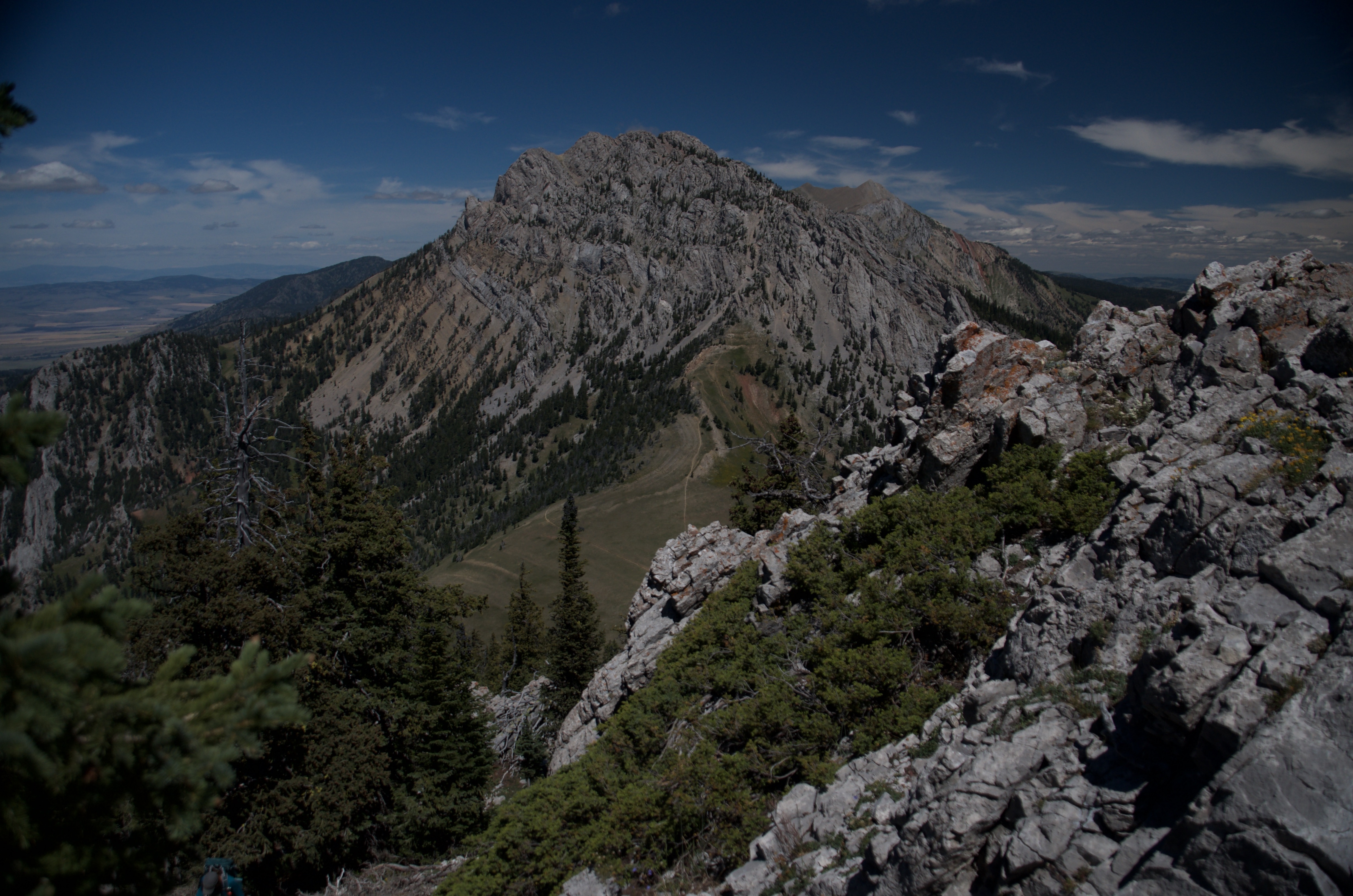 Looking along rocky Bridger Ridge toward a distant peak under partly cloudy sky with scattered subalpine trees