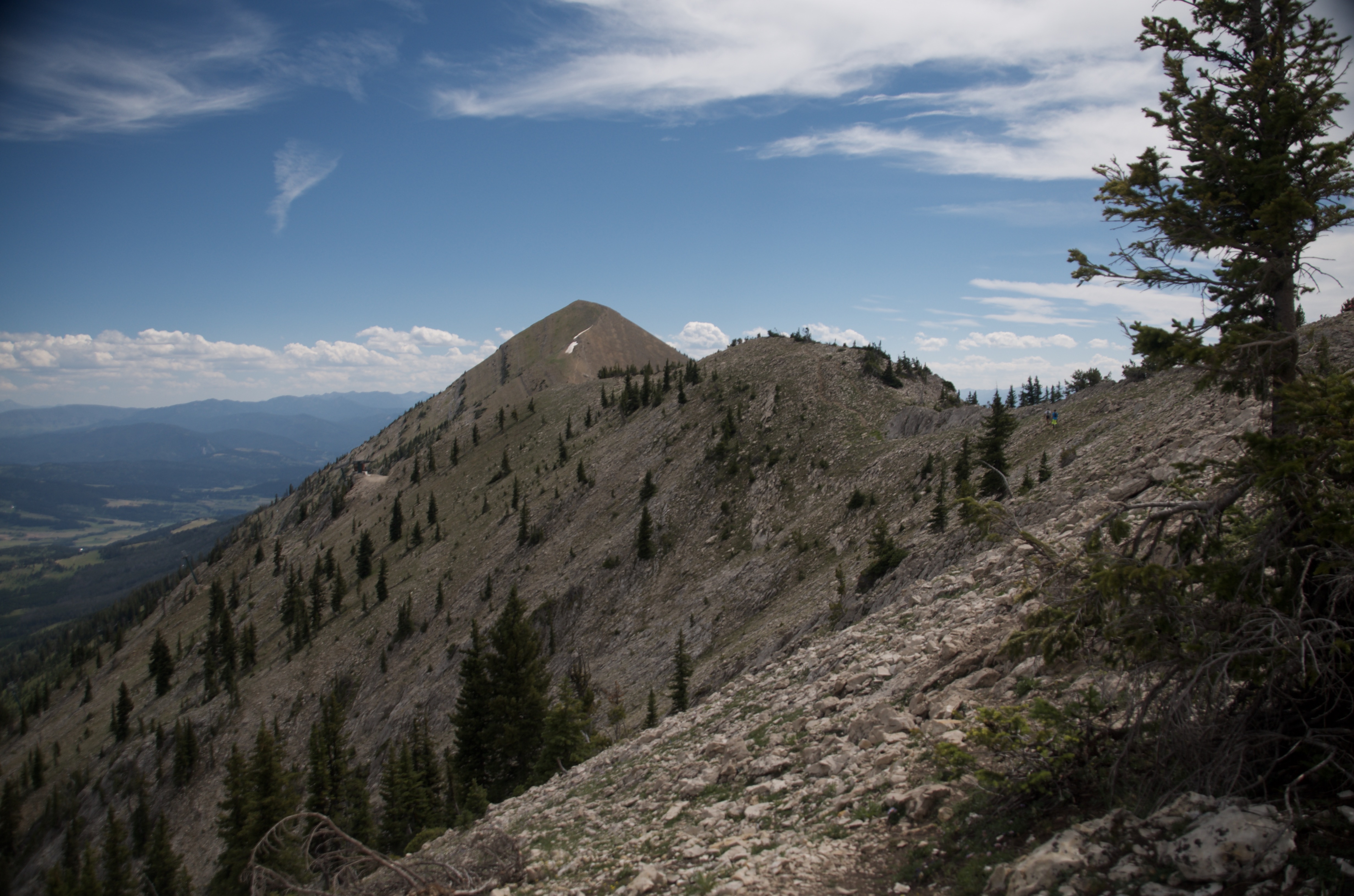 Looking along the rocky ridgeline to a conical Bridger peak ahead under a partly cloudy sky