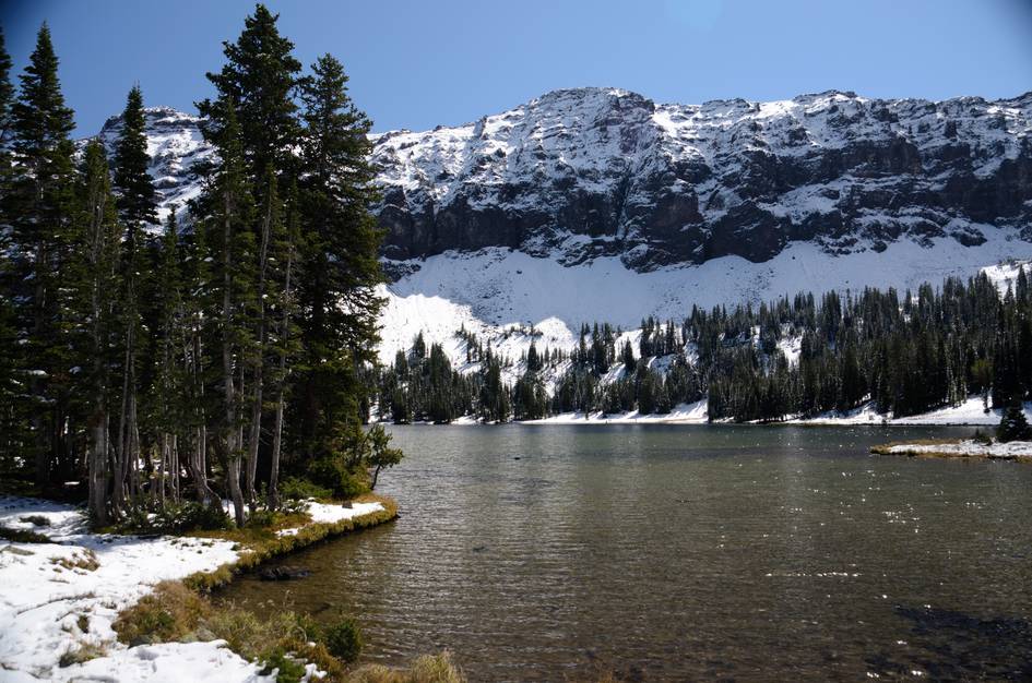 Emerald Lake shoreline with snow-capped cliffs and pine forest