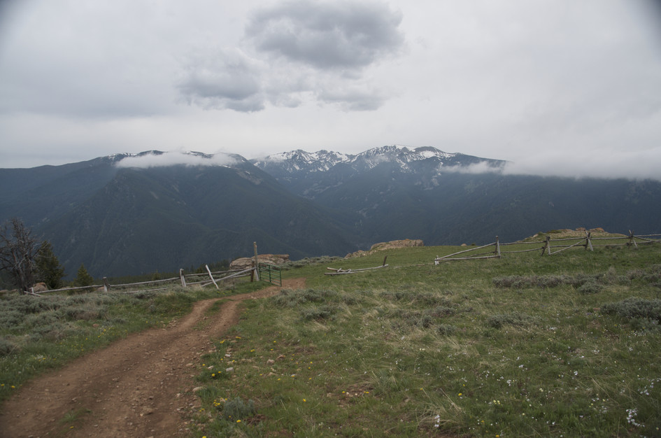 Trail through cattle gate with fence and dramatic stormy mountain backdrop