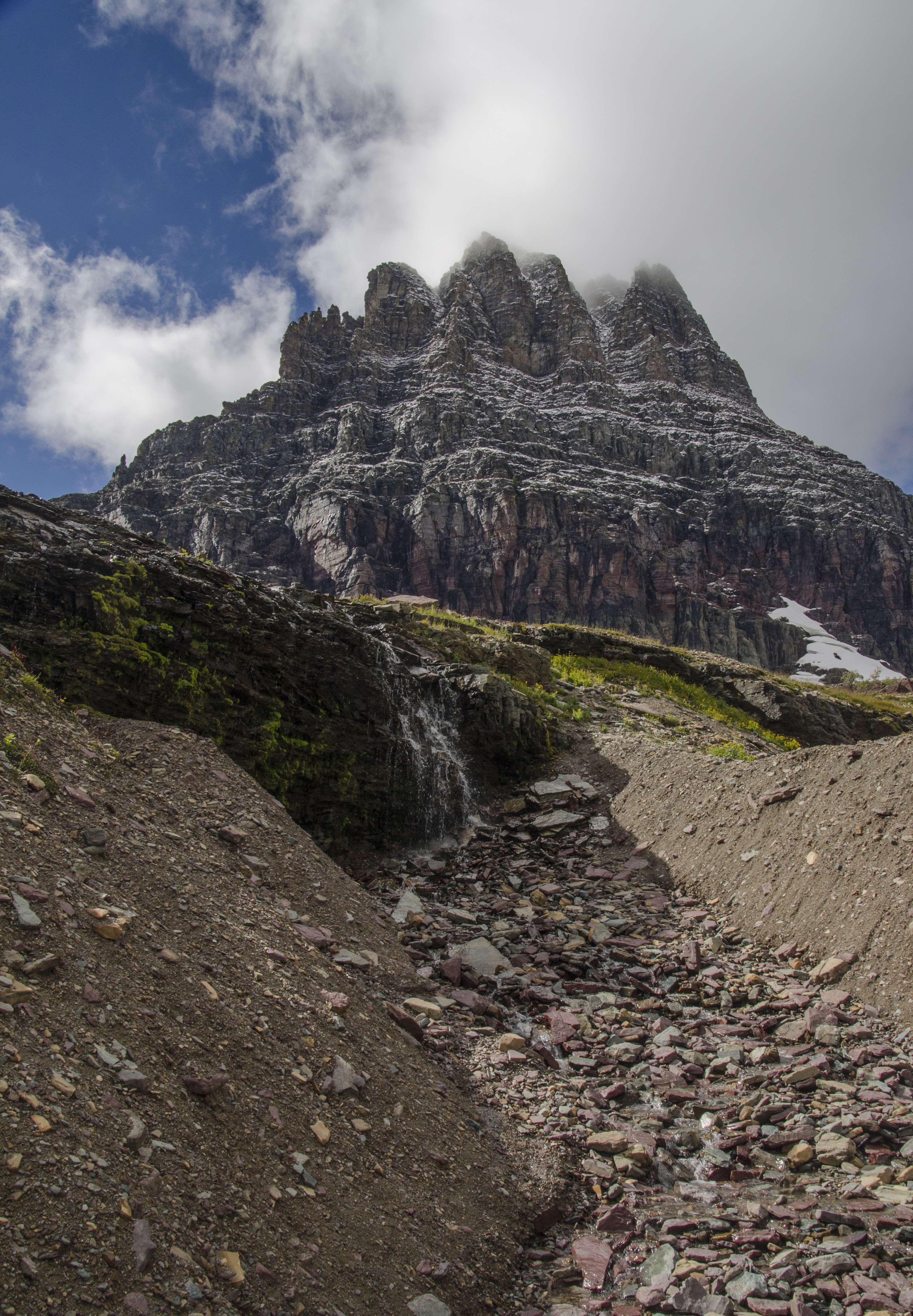 Rocky peak with waterfall streaming down scree slope beneath clouds