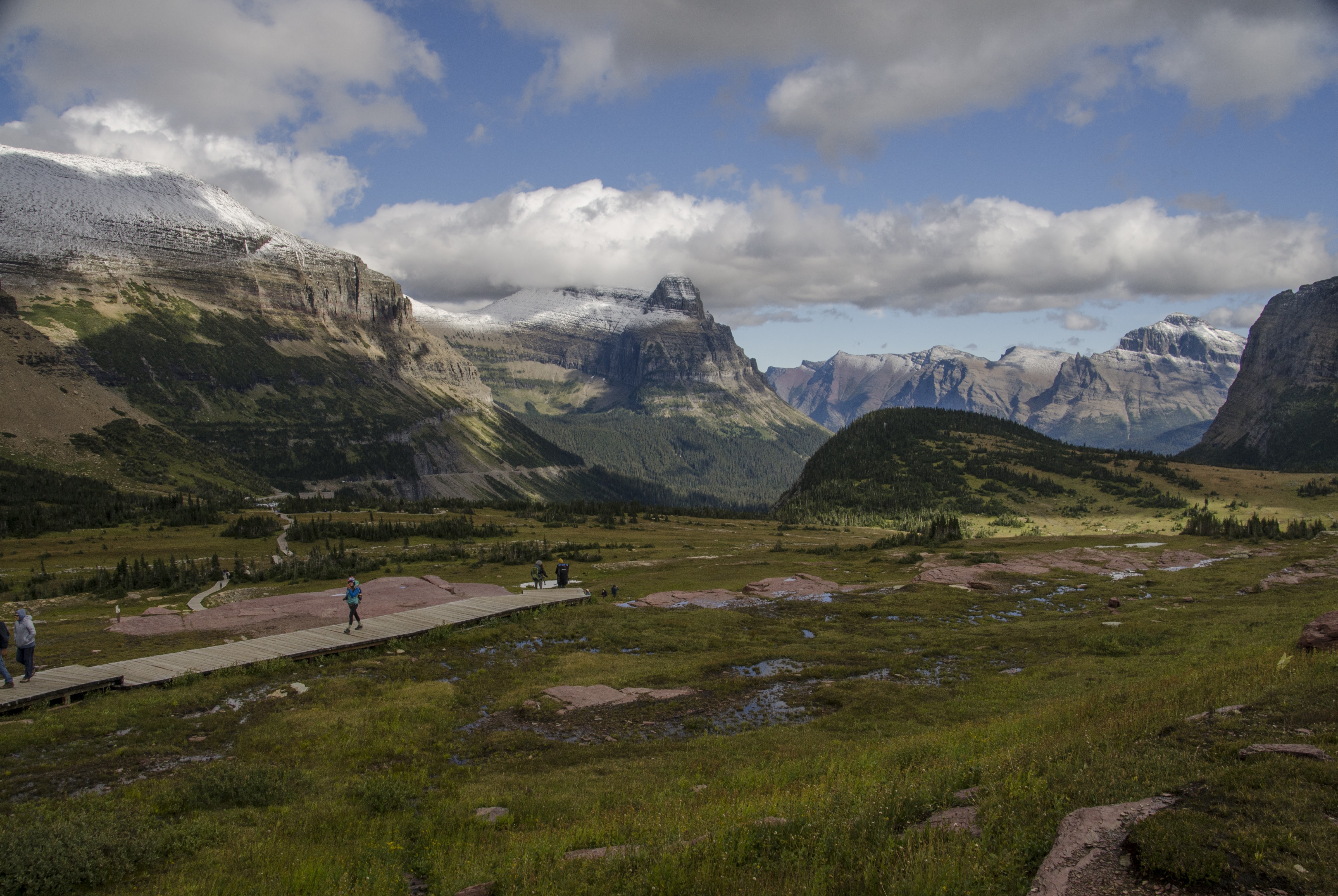 Wide boardwalk panorama with hikers and mountains surrounding alpine meadow