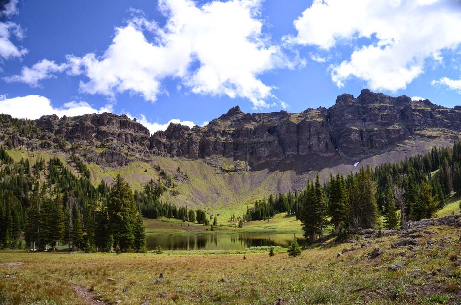 Hyalite Lake in alpine basin surrounded by green meadow with dramatic rocky cirque cliffs