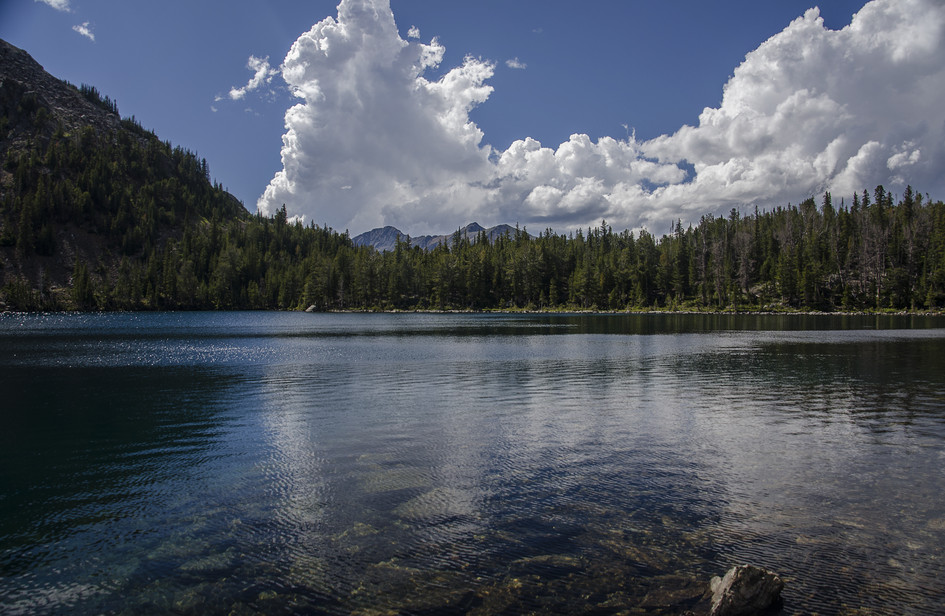 Louise Lake reflecting dramatic clouds with forested shore and distant peaks