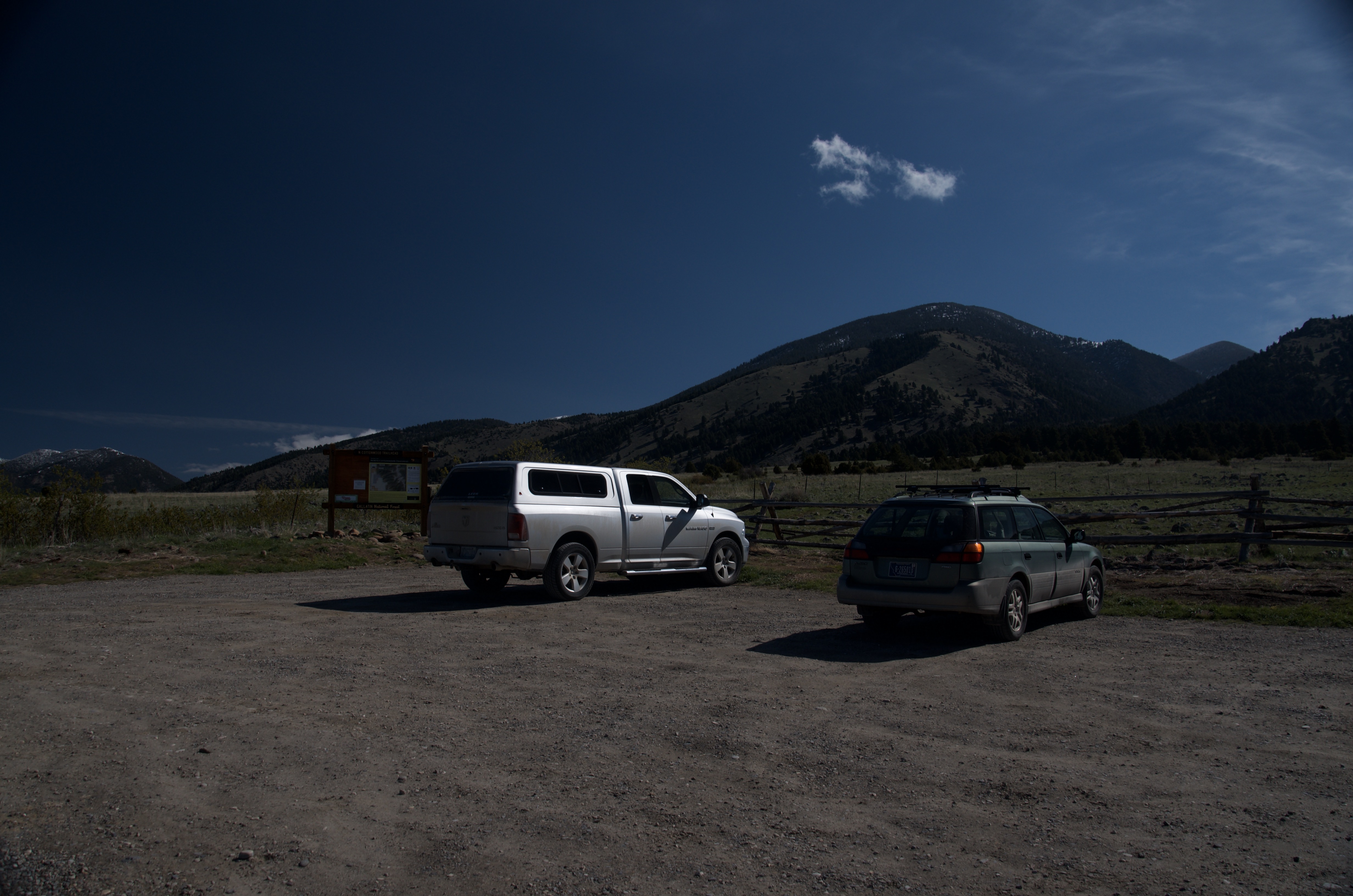 Small gravel parking area with two vehicles and Gallatin National Forest trailhead kiosk, Bridger Range peaks visible behind