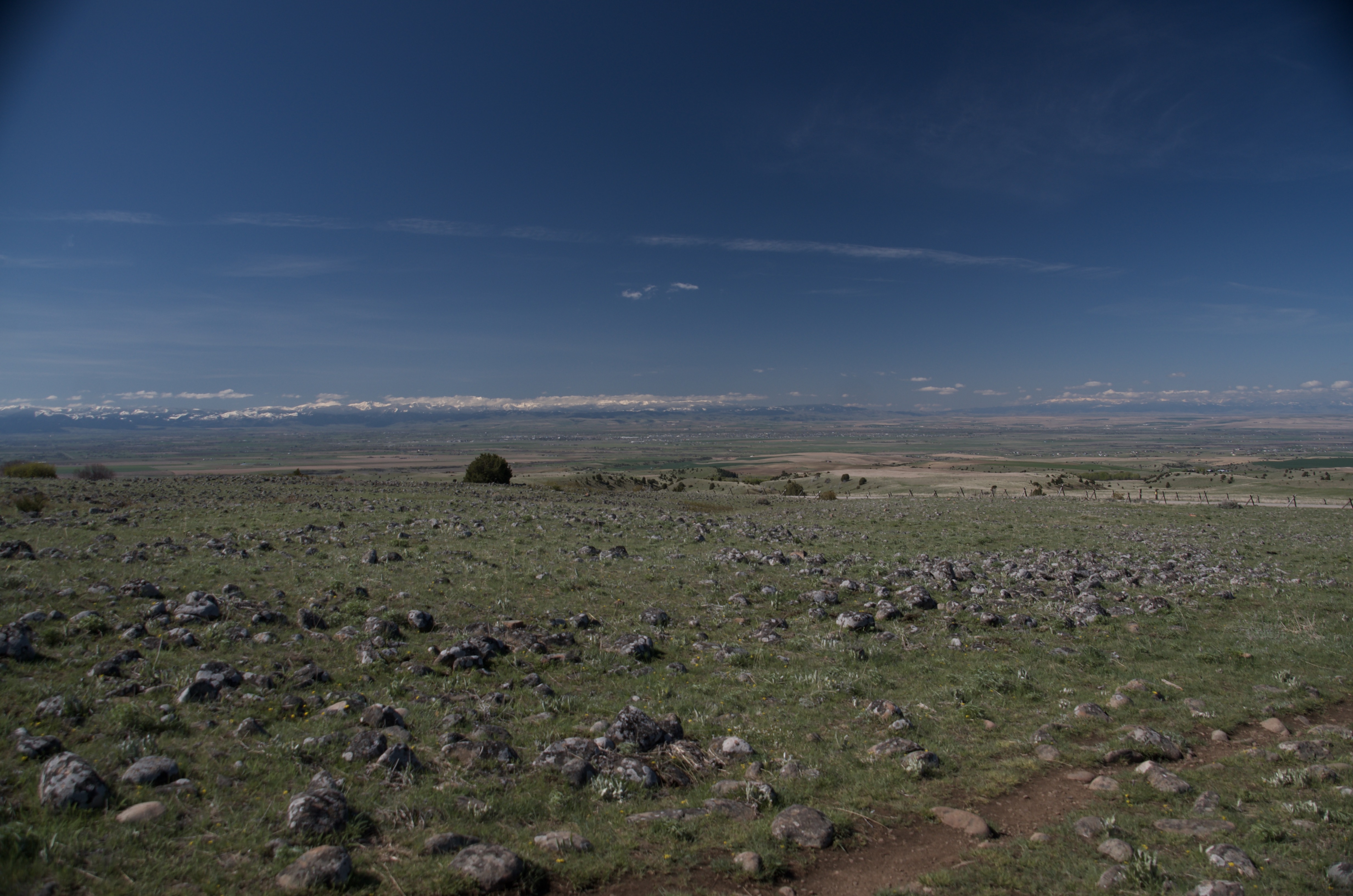 Open rocky meadow terrain with scattered stones and sweeping Gallatin Valley view under deep blue sky