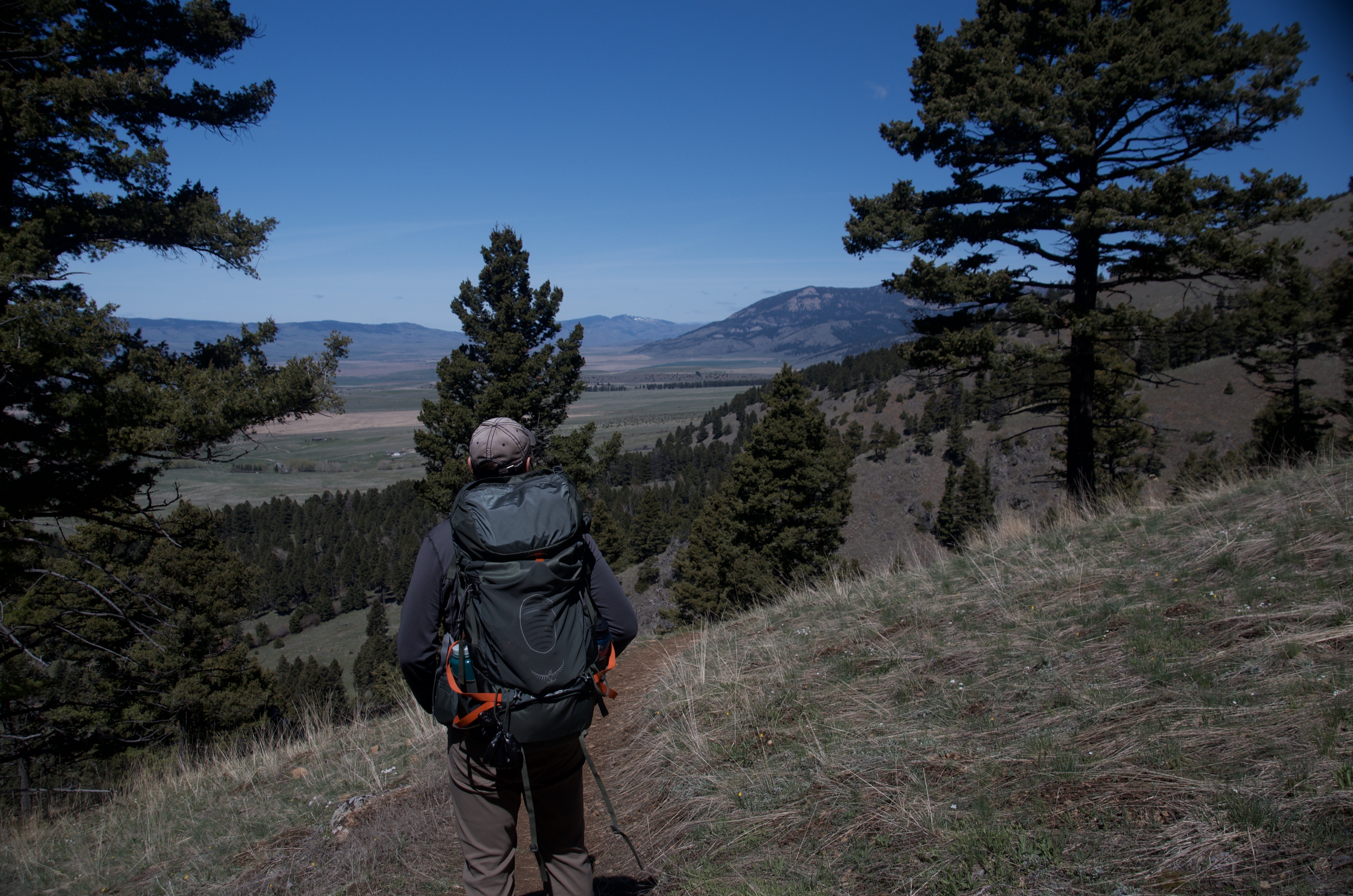 Hiker with large backpack pausing on trail to look out over wide Gallatin Valley and distant mountain ranges