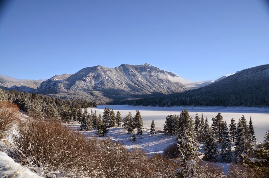 Frozen Hyalite Reservoir with snow-covered mountains and pine trees