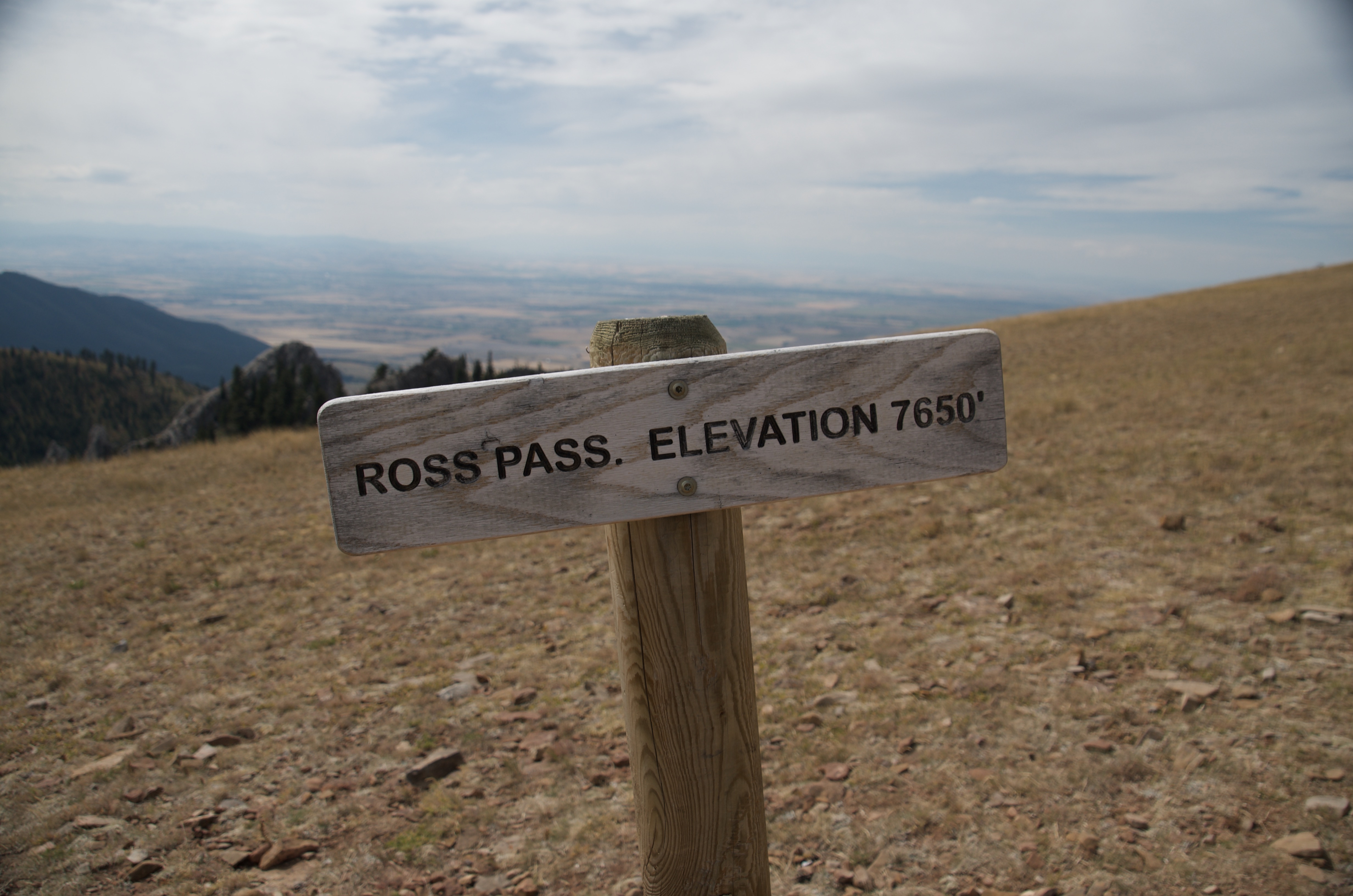 Wooden sign reading Ross Pass Elevation 7650 feet with open Gallatin Valley visible behind