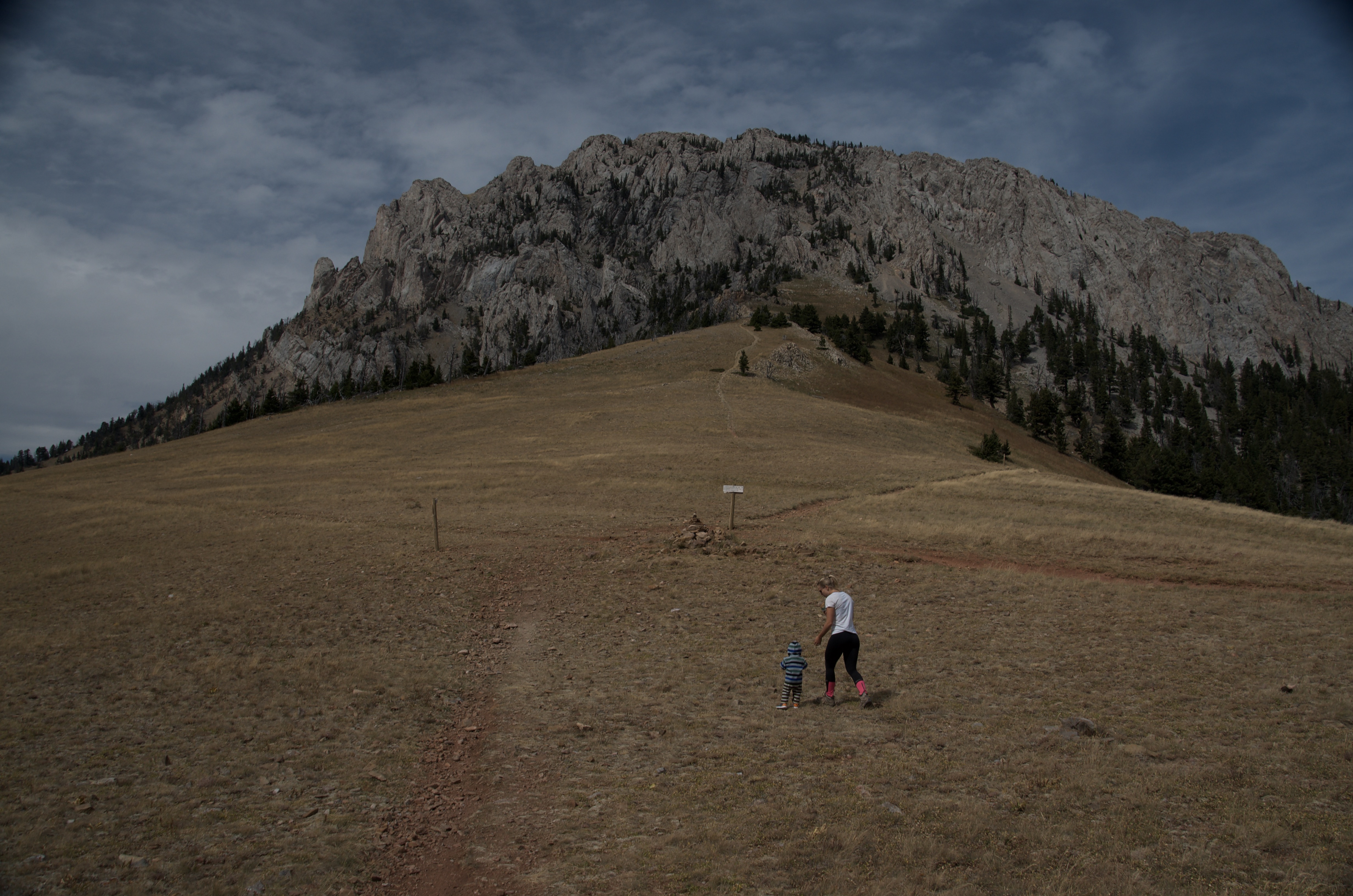 Adult and small child at Ross Pass with jagged limestone wall of Ross Peak rising behind them