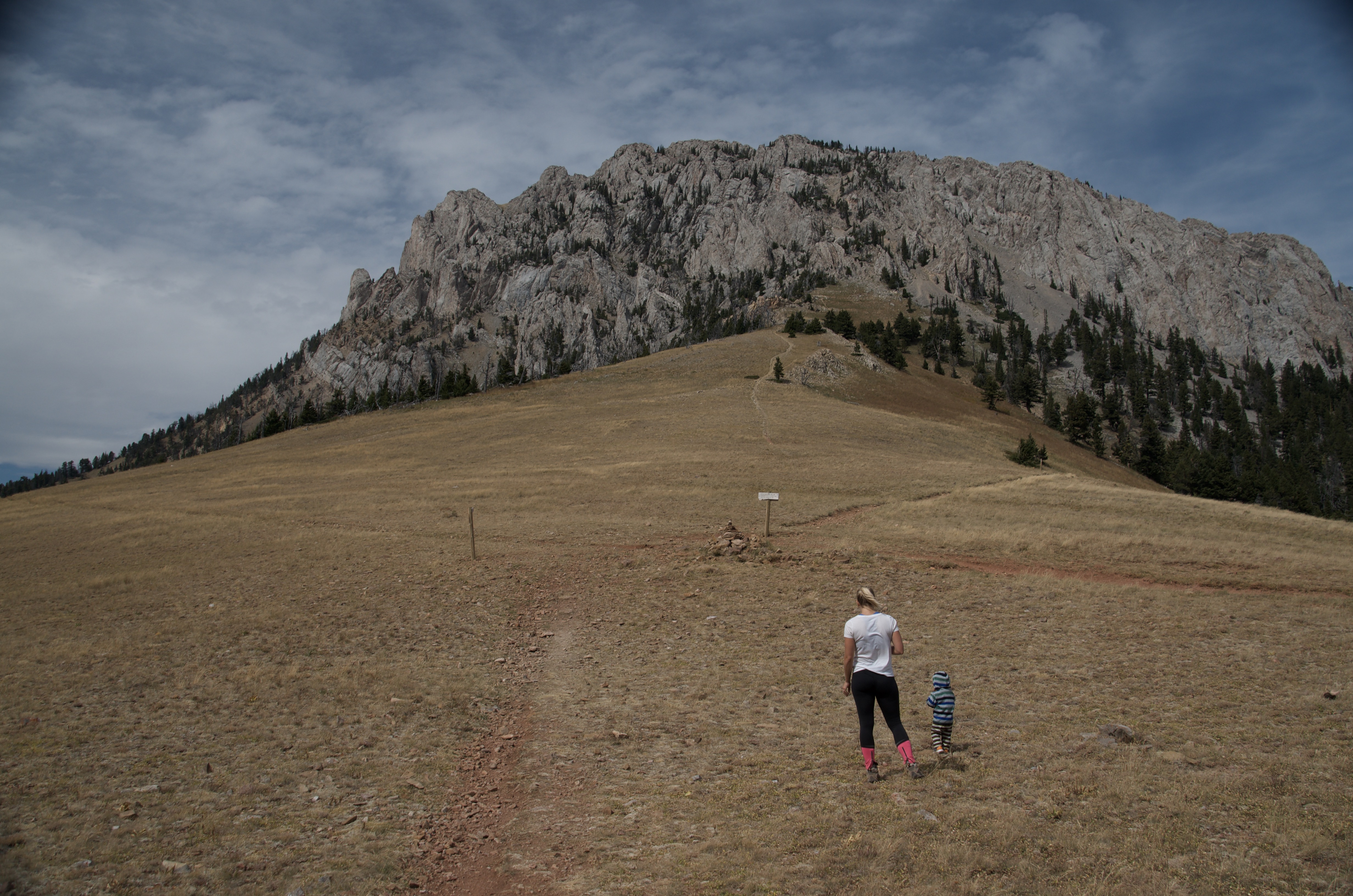 Parent and young child walking toward Ross Pass sign with limestone cliffs in background